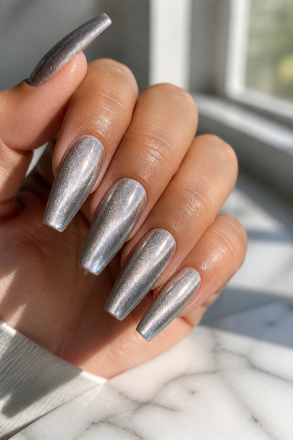 Close-up of icy cat-eye silver coffin nails on a real hand under window light