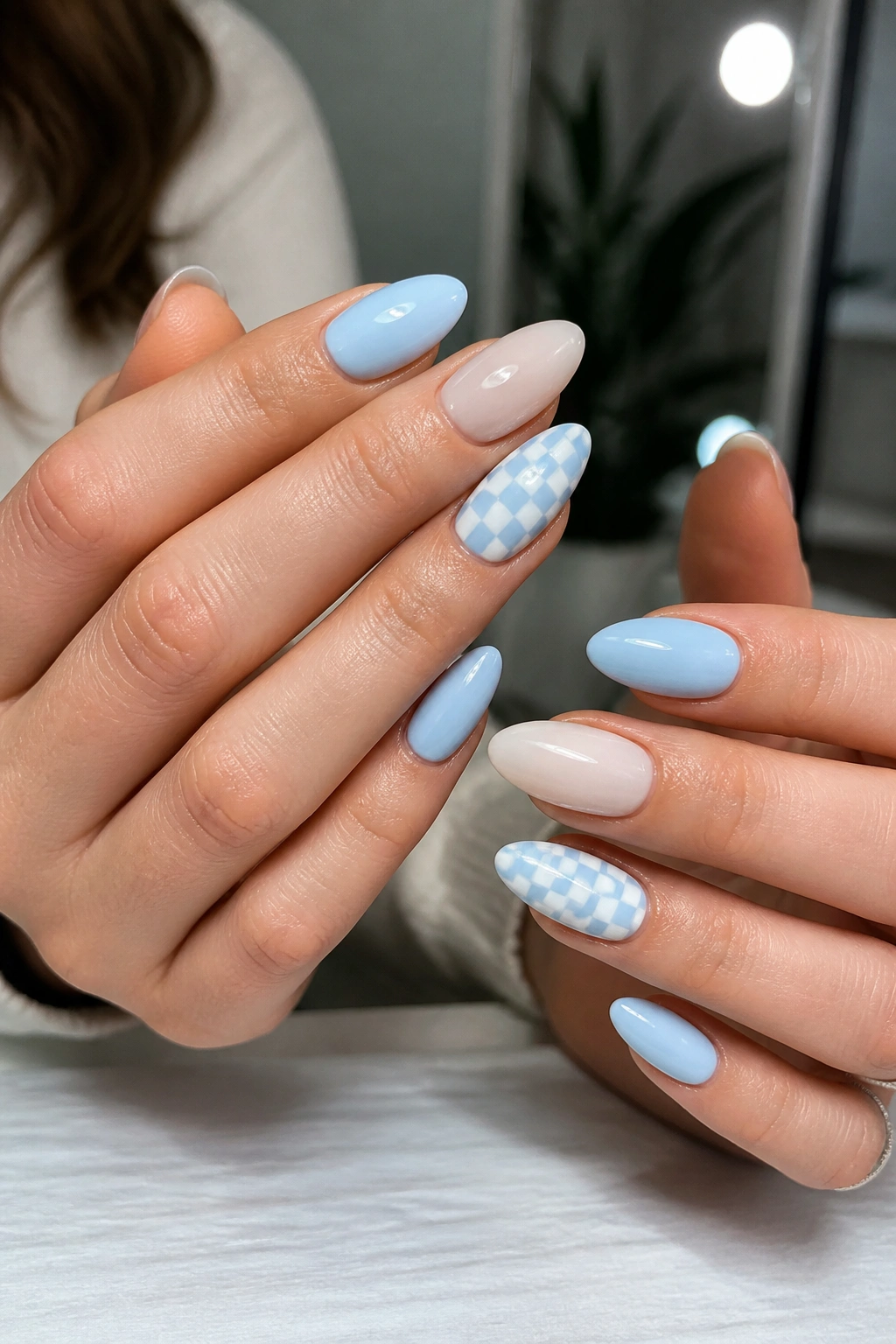 Close-up of almond nails with a checkerboard accent nail in blue and white