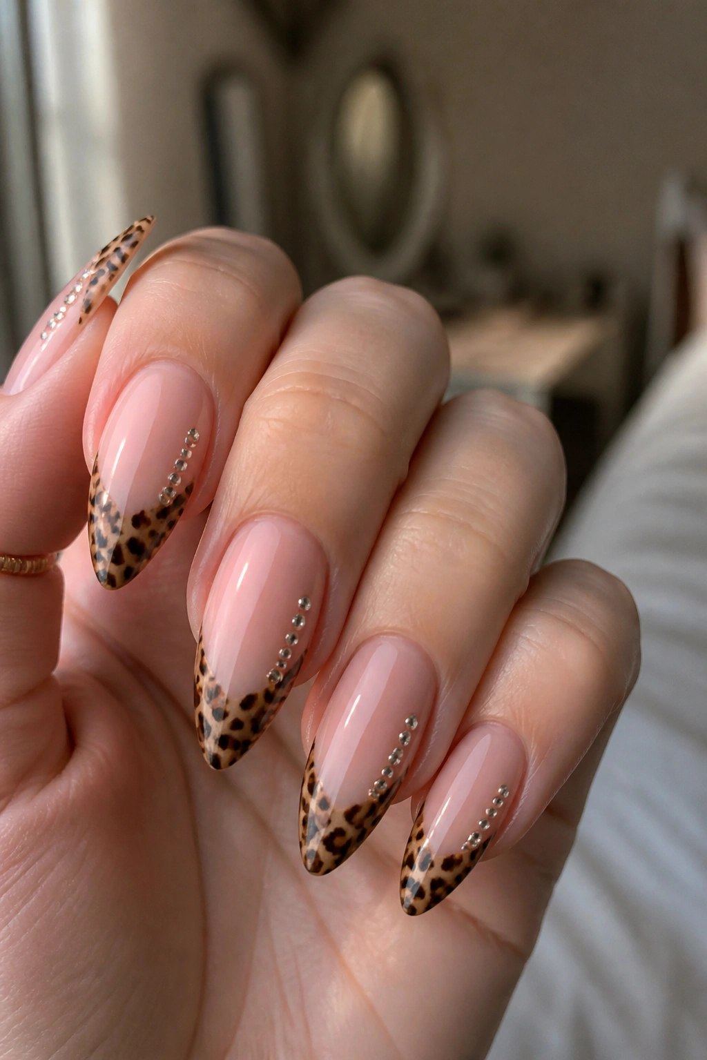 Close-up of nude almond nail with cheetah patch and tiny rhinestones along one side on a real hand