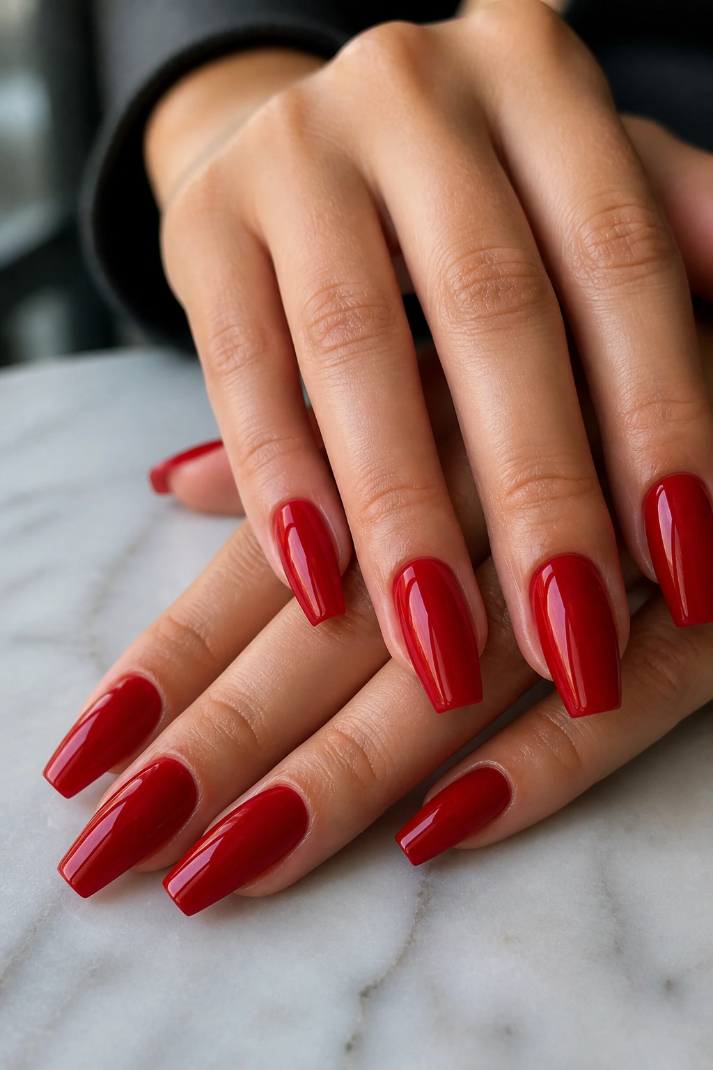 Close-up of hands with cherry red cream coffin nails on marble