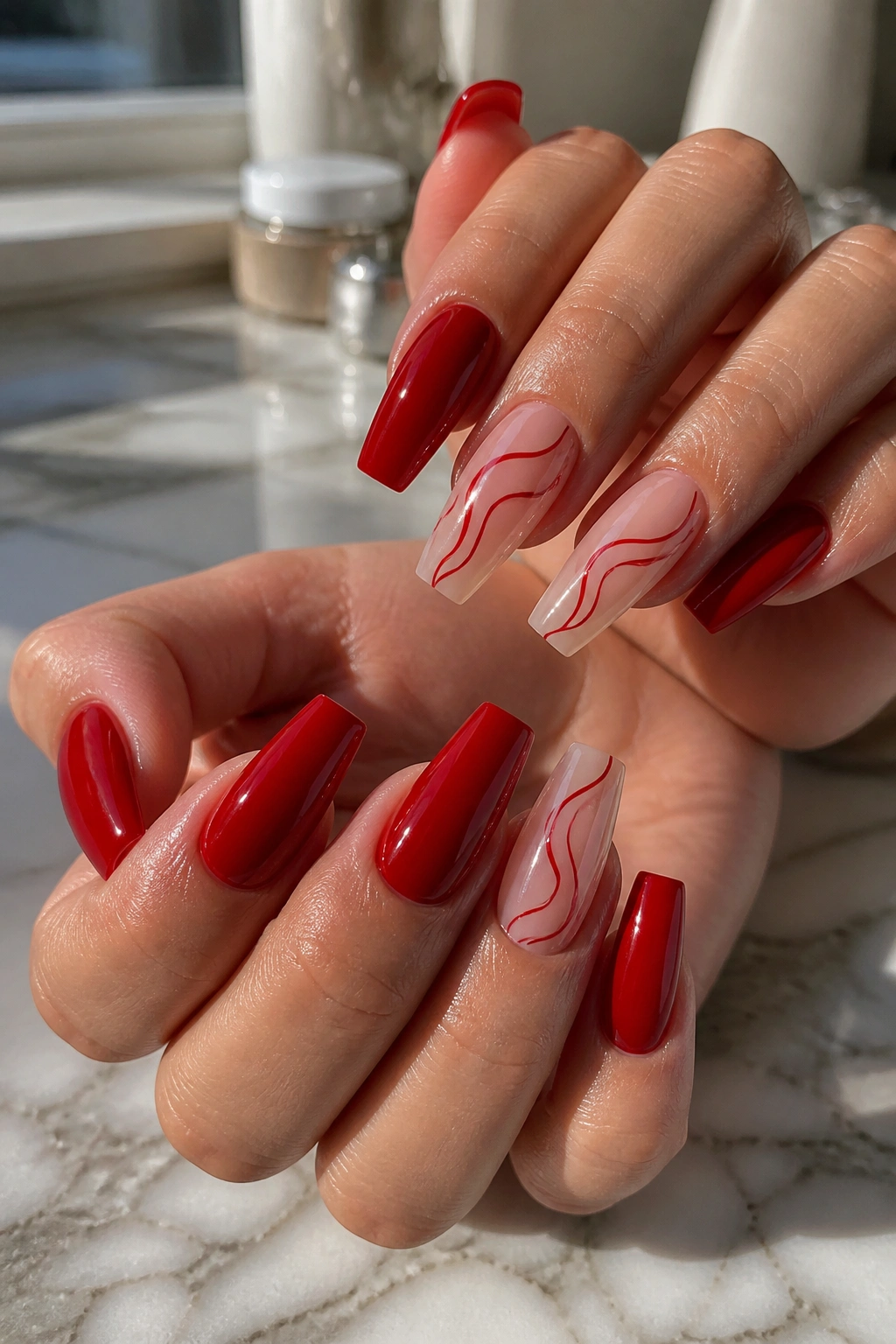 Close-up of hand with coffin nails showing cherry-red solids and swirl accents in a salon setting
