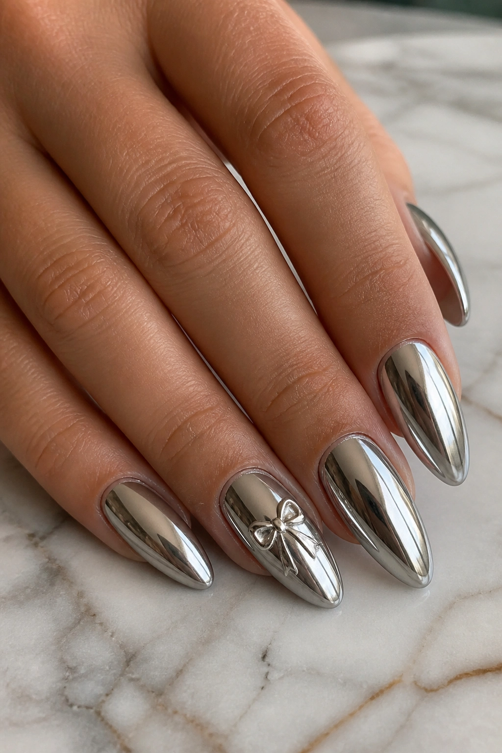Close-up of chrome almond nails with silver edges and a bow accent