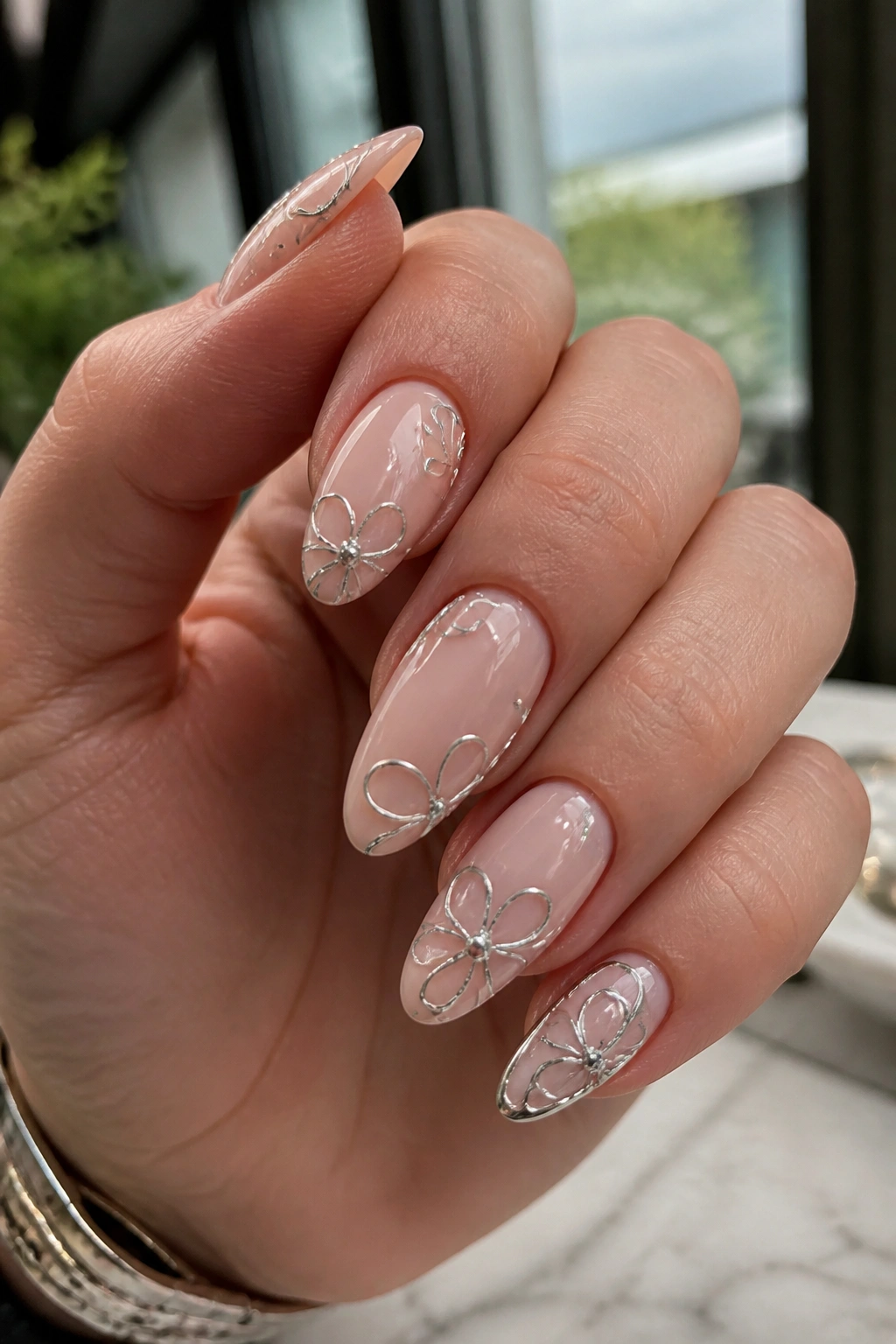 Close-up of nude almond nails with chrome petal outlines