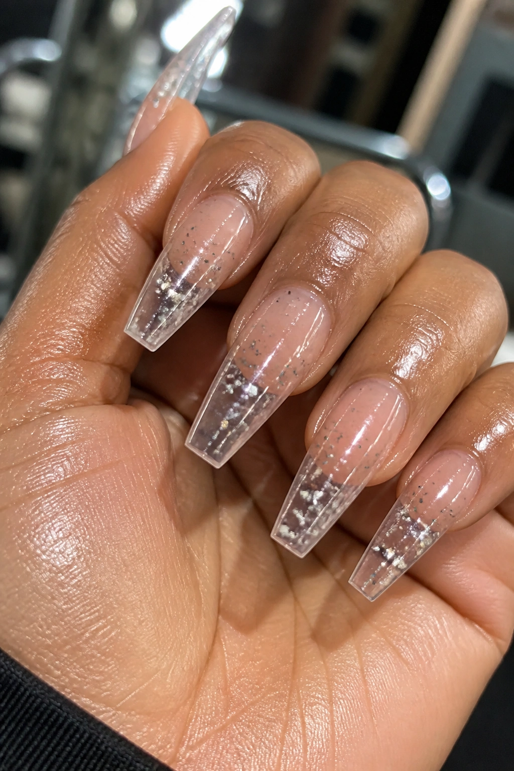 Clear jelly coffin nails with loose silver glitter on a real hand