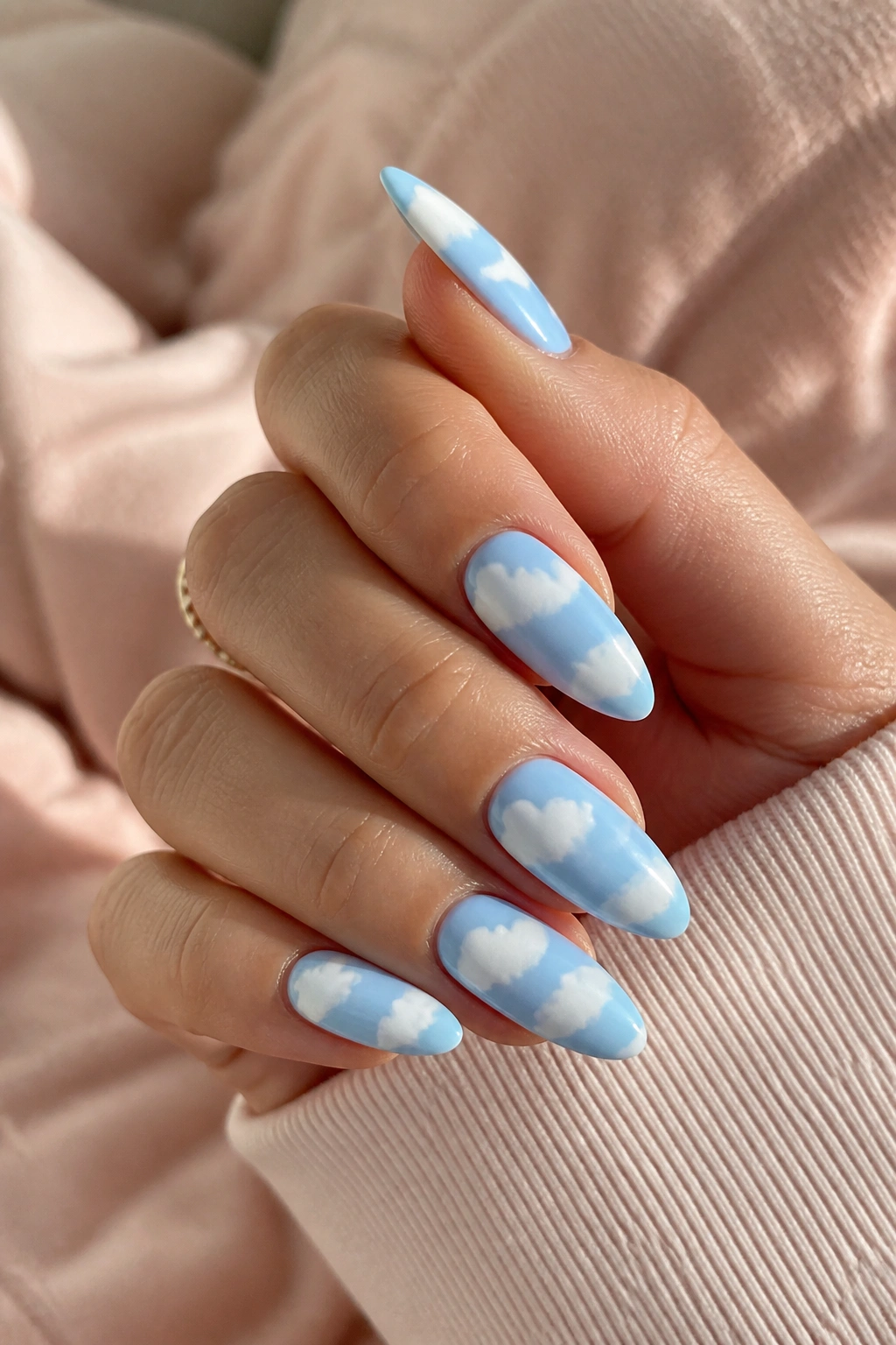Close-up of milky blue almond nails with white cloud art on a real hand