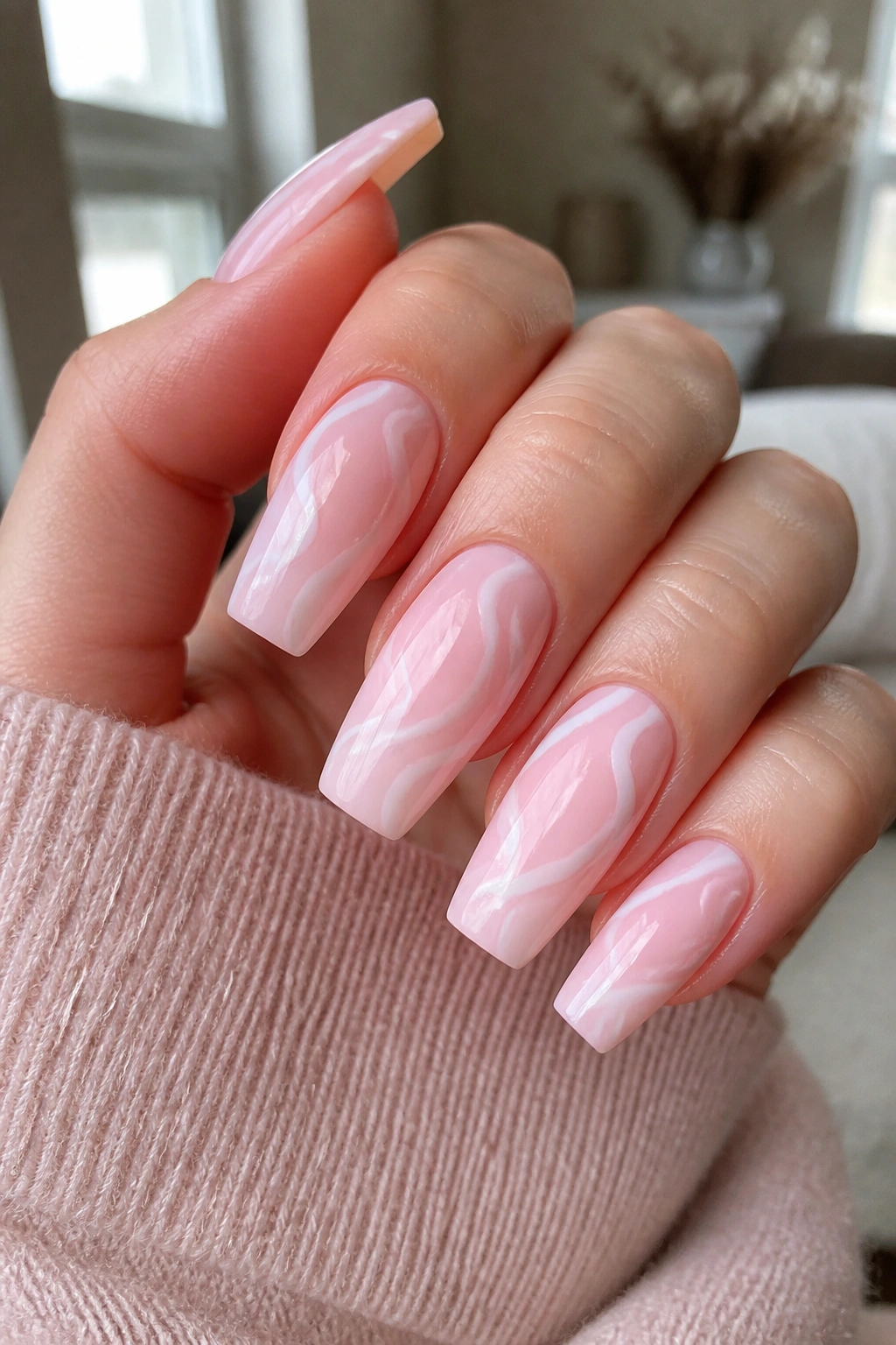 Close-up of soft pink coffin nails with white swirl art on real hand
