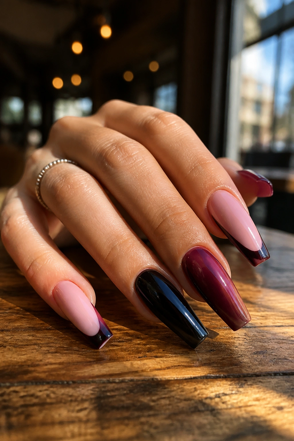 Close-up of pink and dark coffin nails on a real hand with glossy finish in a warm cafe setting