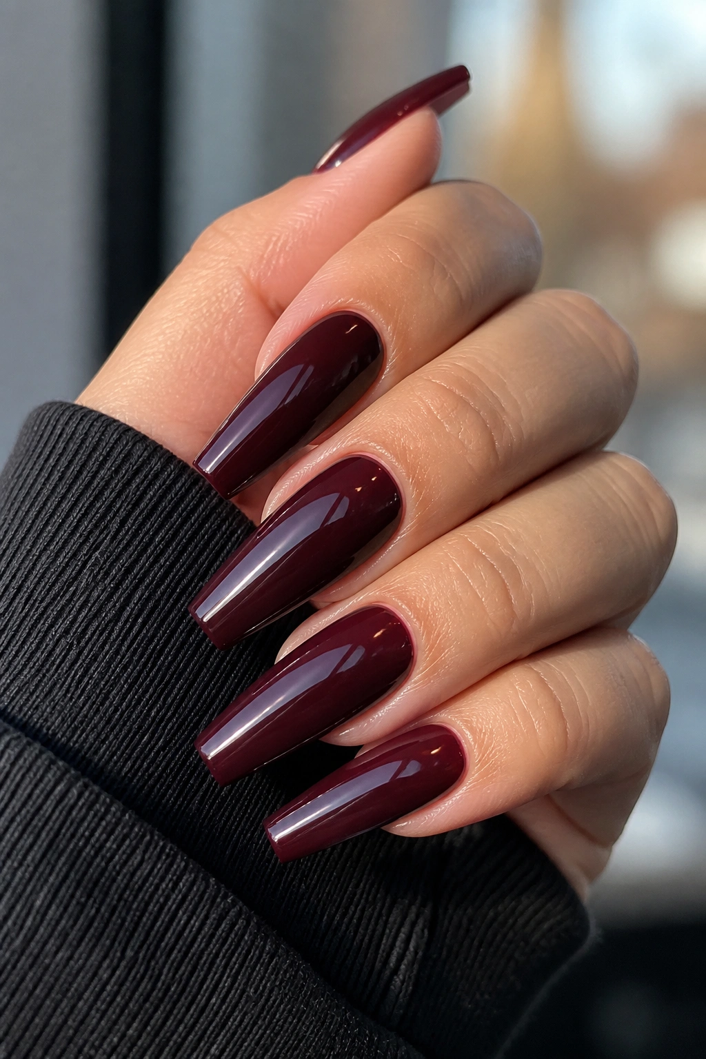 Close-up of a hand showing coffin nails with sharp tapered tips in dark burgundy.