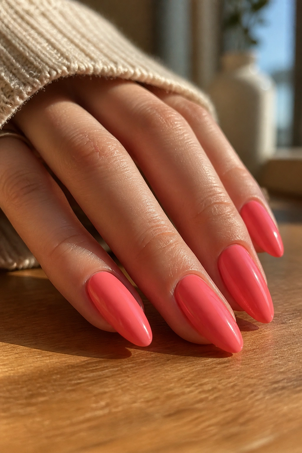 Close-up of a real hand with coral-pink almond nails glossed to perfection.