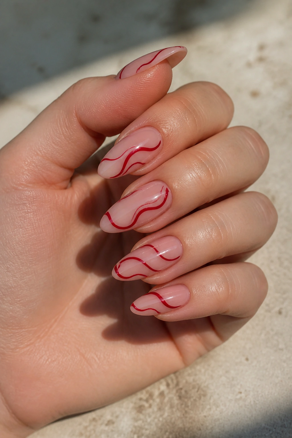 Close-up of real hand with almond nails featuring crimson swirl designs on nude base