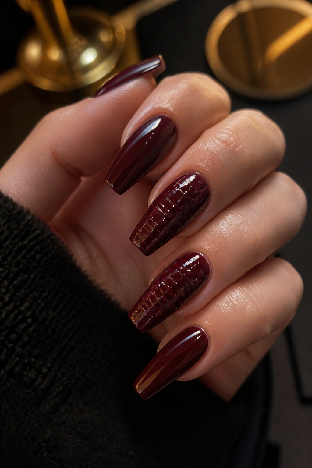 Close-up of croc-stamped burgundy coffin nails with patent shine on a real hand