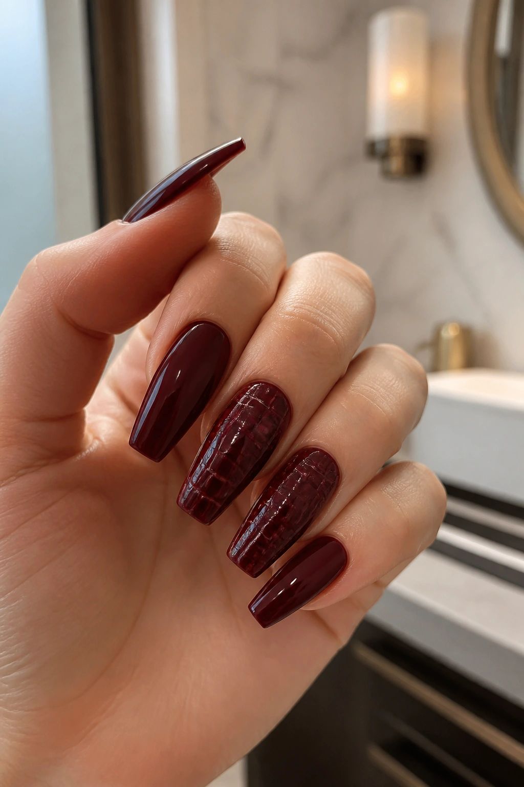 Close-up of hand with croc-embossed maroon accent nails on a hand.