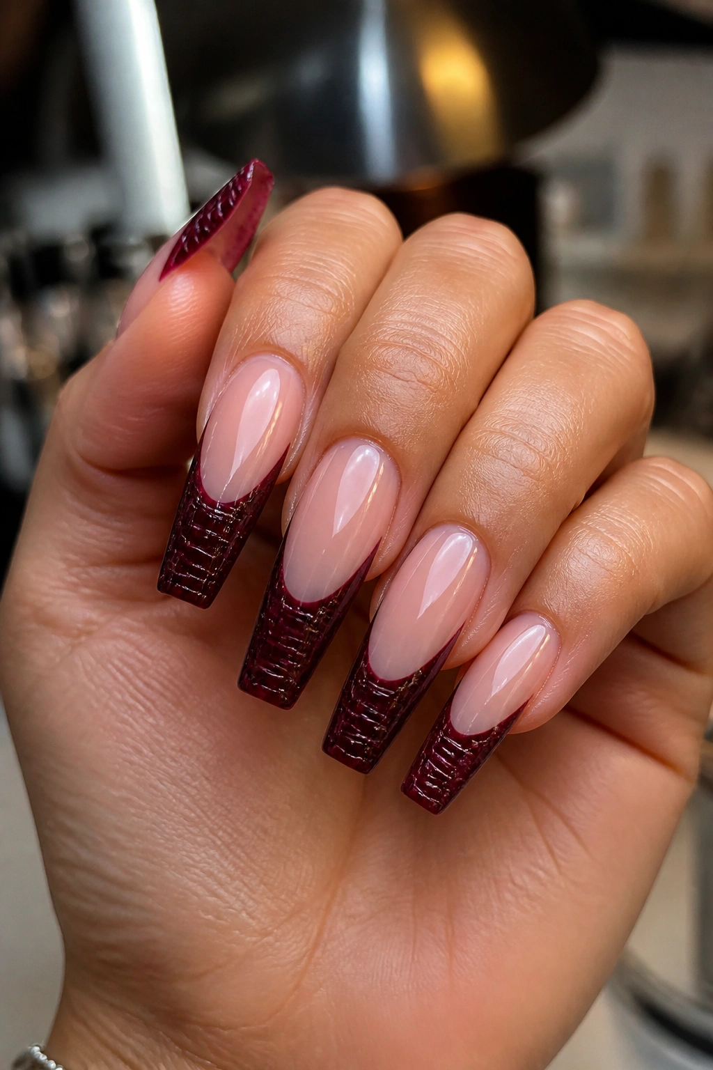 Close-up of croc-embossed merlot tips on a clear nude base on a real person's nails.