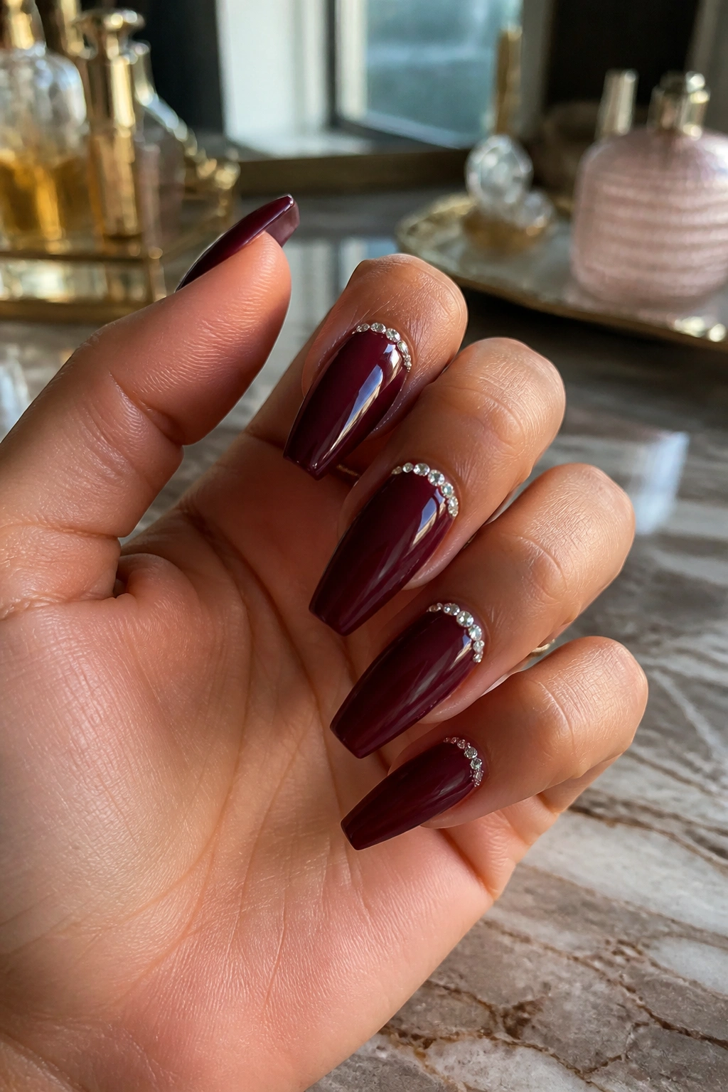Close-up of glossy maroon coffin nails with a crystal cuticle line on accent nails.