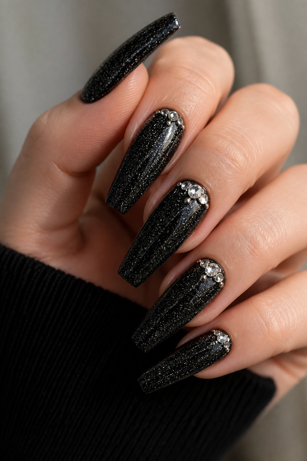 Nails with black glitter and crystal accents close-up on a real hand