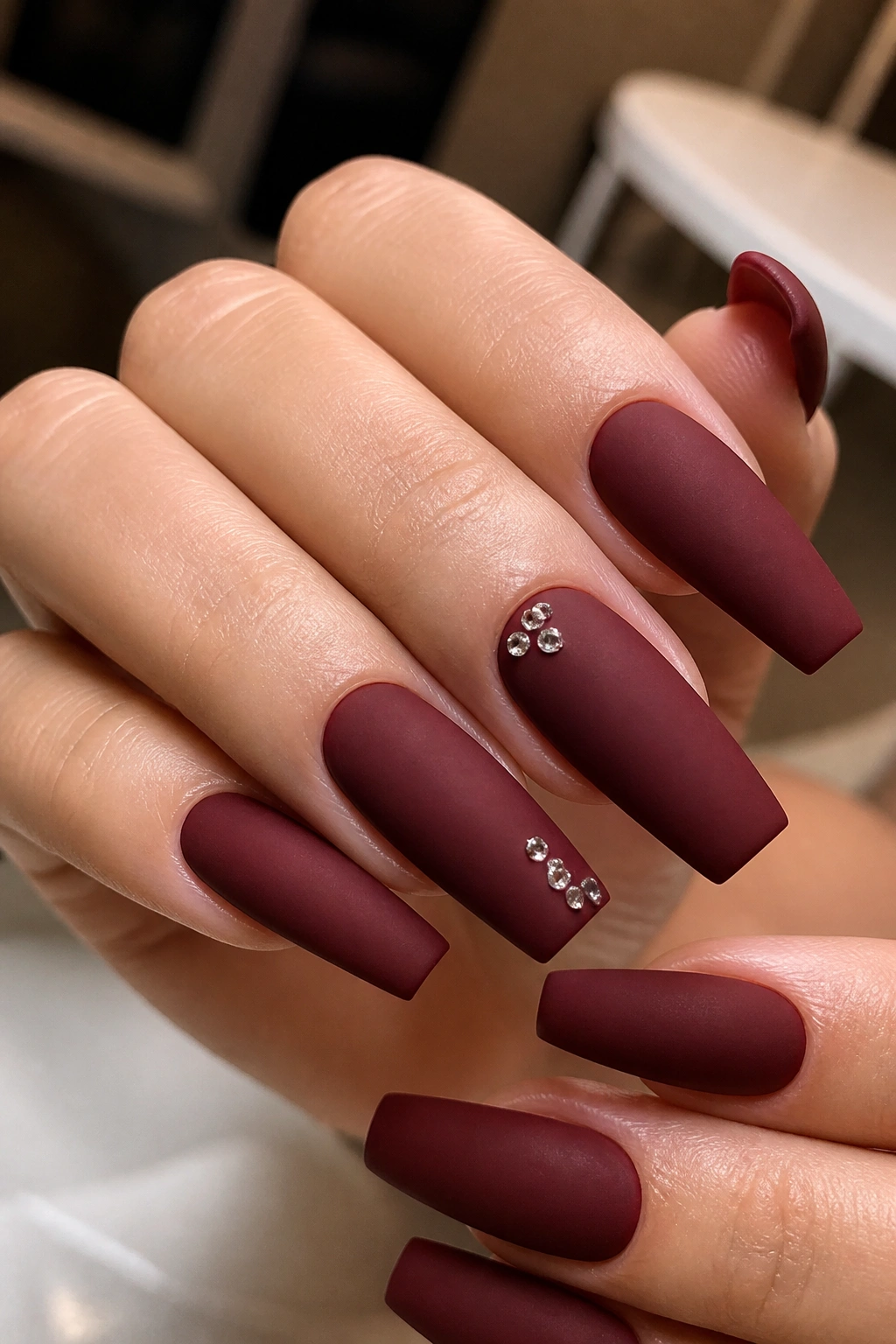 Close-up of dark cherry matte nails with tiny rhinestone clusters