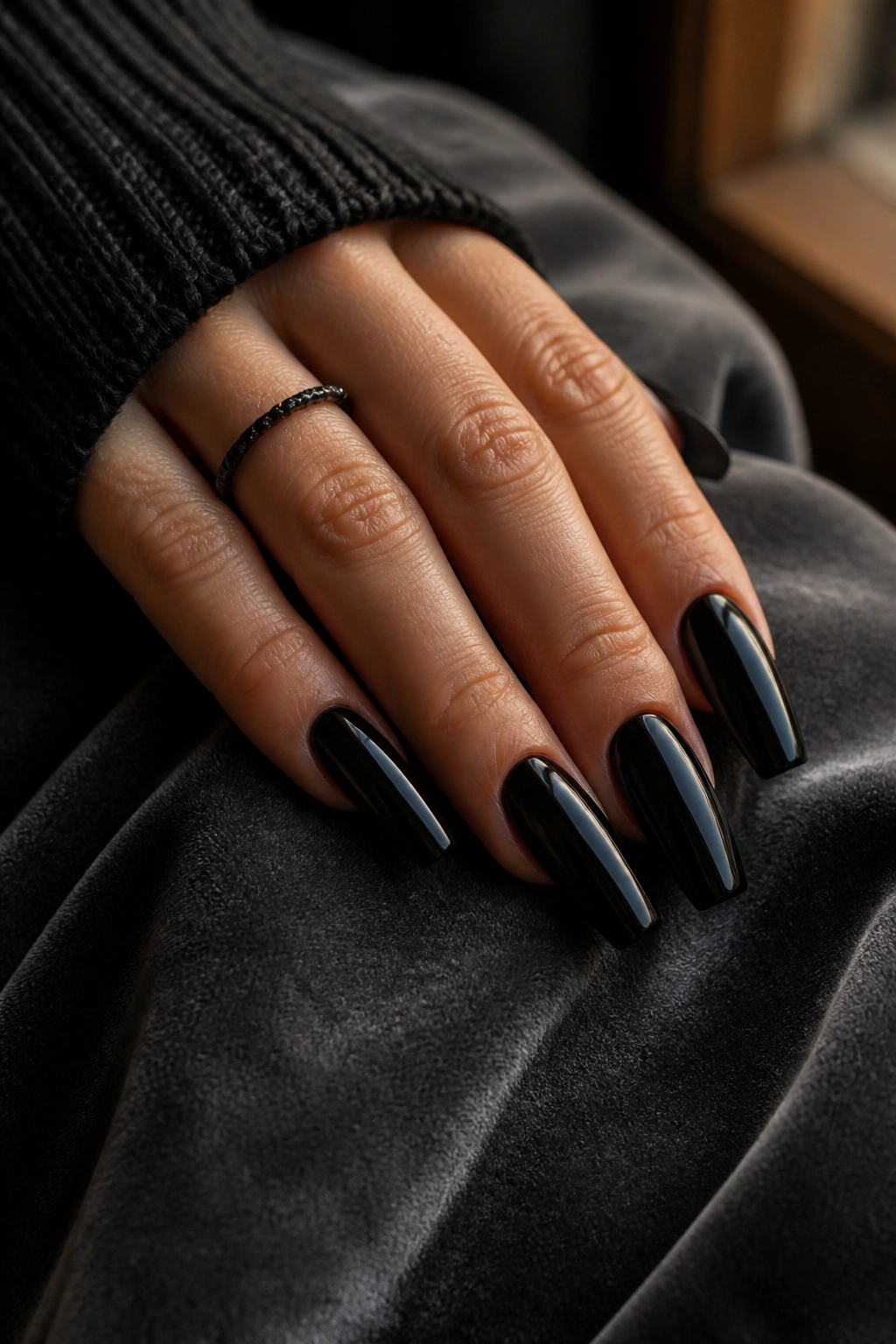 Close-up of a real hand with dark coffin nails in moody window-lit lighting