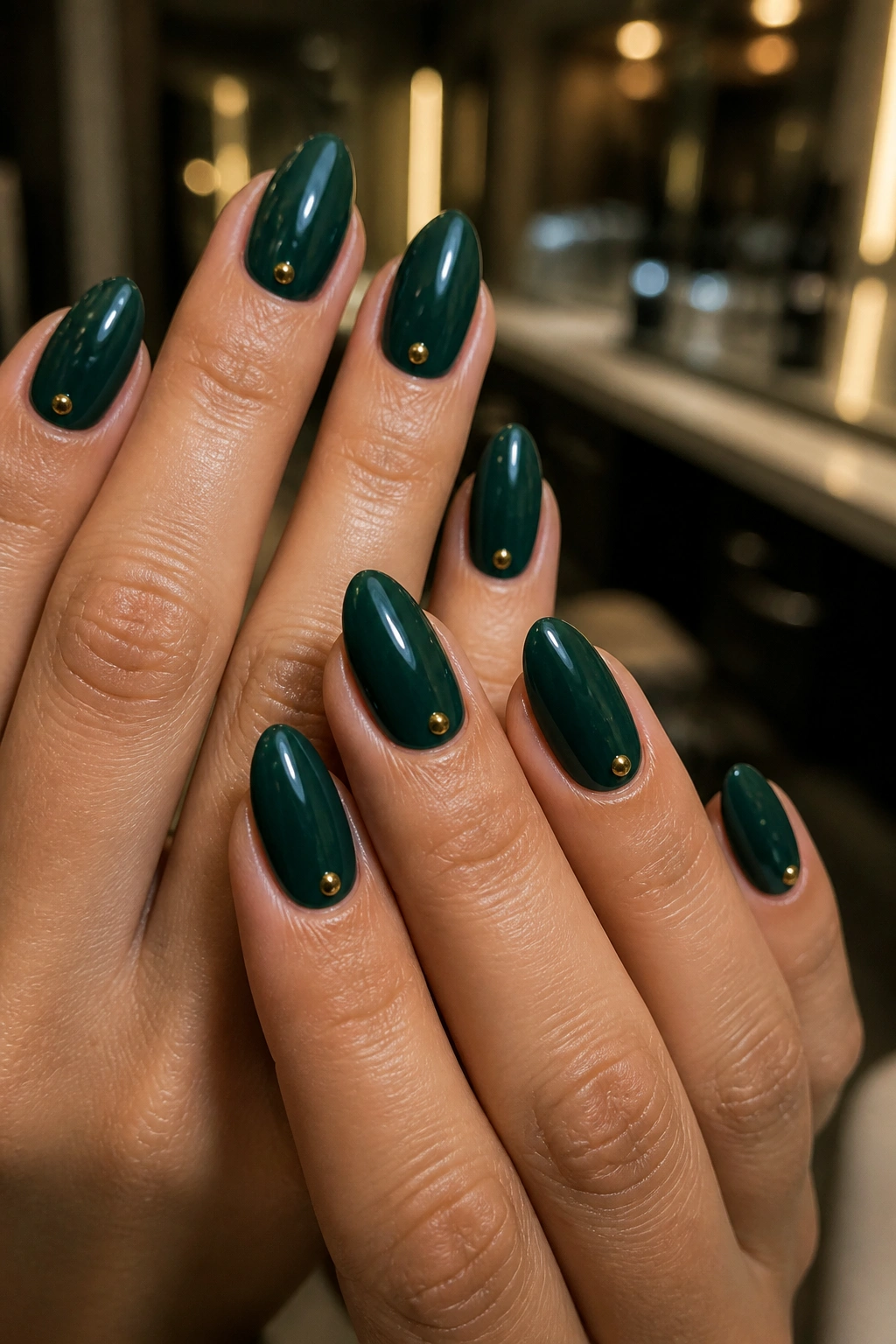 Close-up of dark green almond nails with small gold studs near the cuticle on a real hand