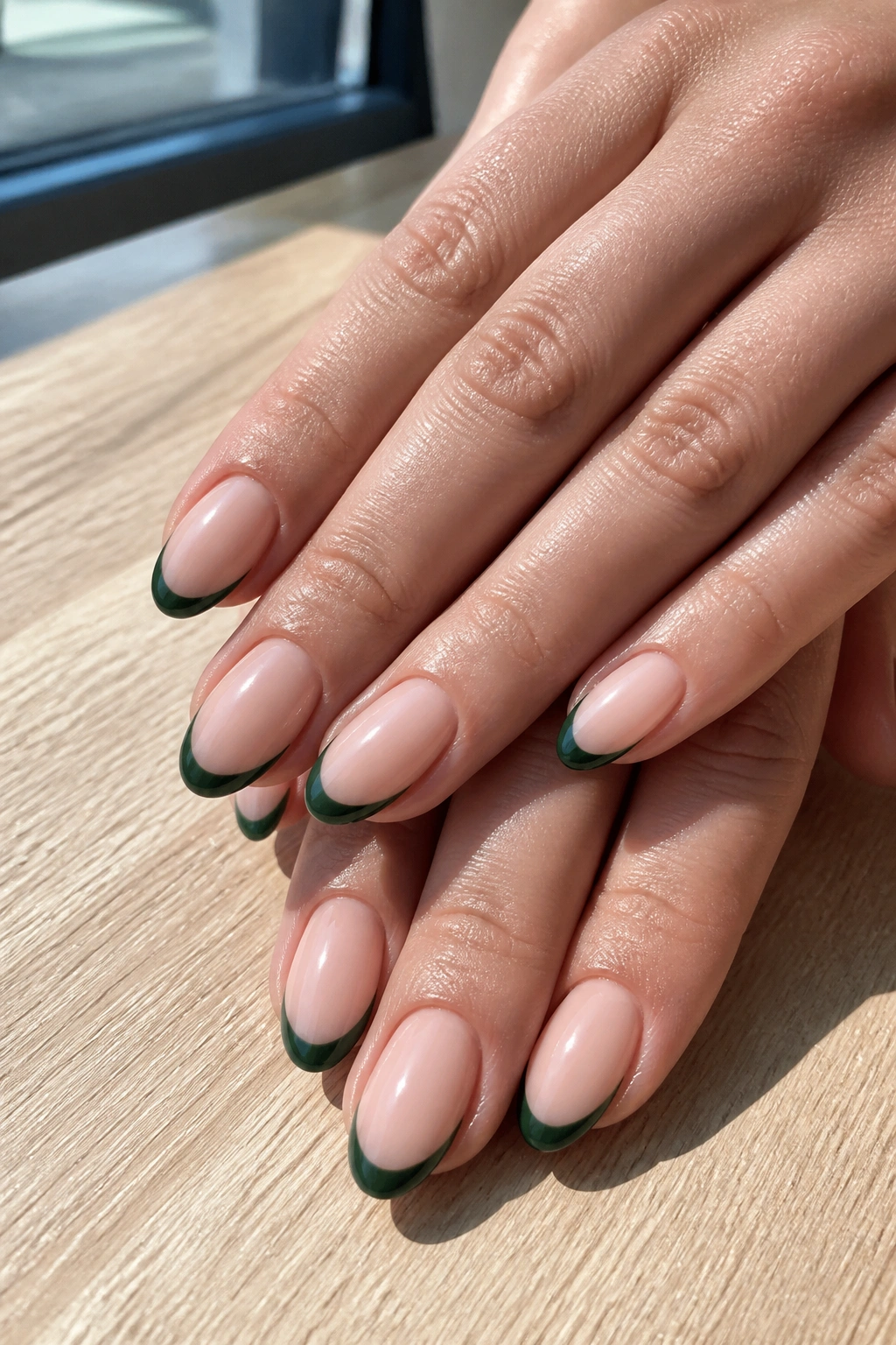 Close-up of almond nails with nude base and dark green tips on real hands