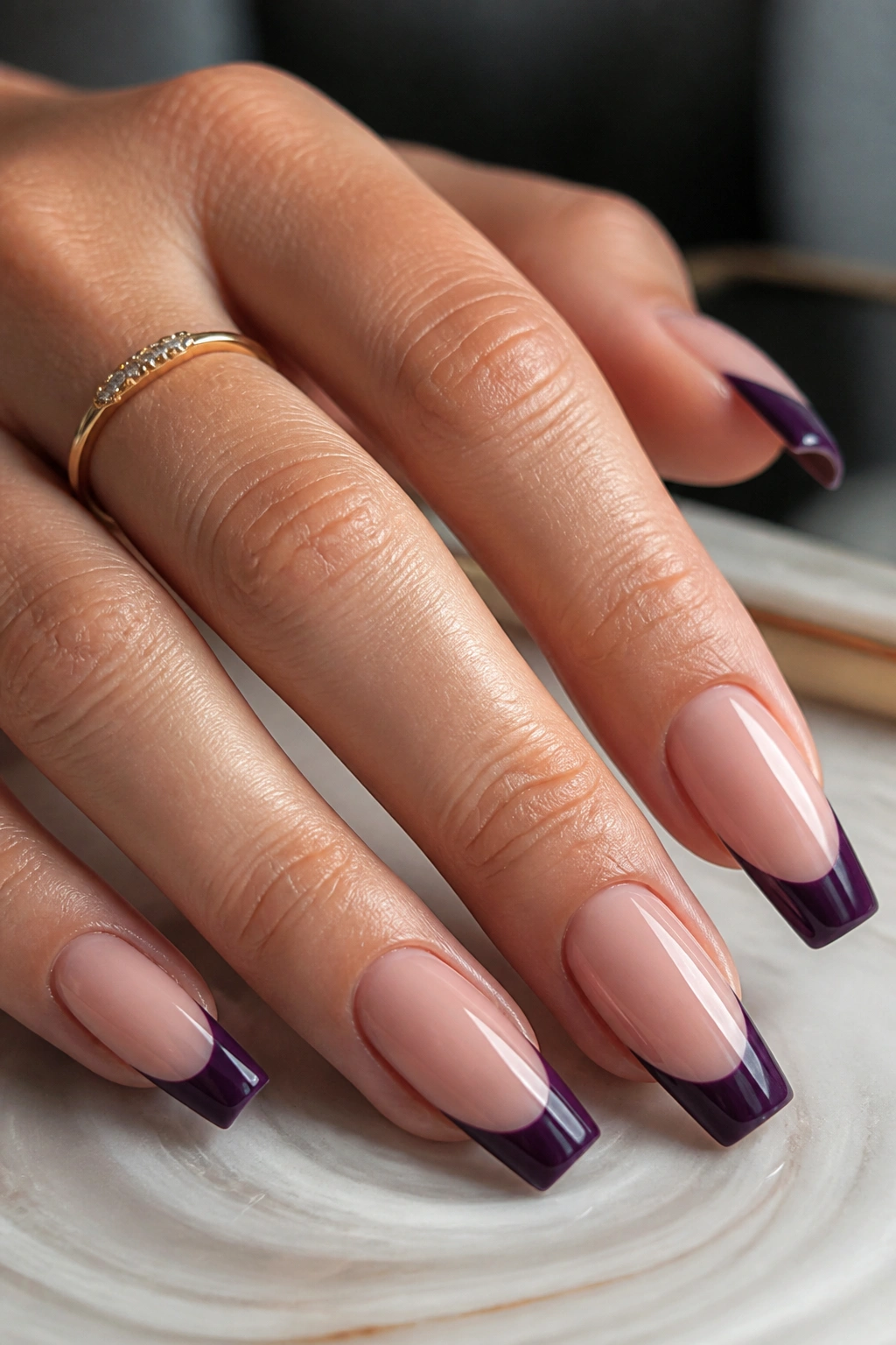 Close-up of nude coffin nails with dark purple French tips on a real hand
