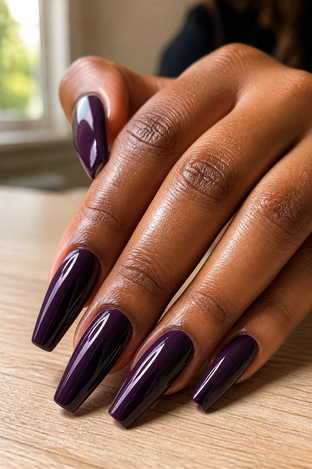 Close-up of dark purple coffin nails on a real hand with glossy finish in warm indoor light