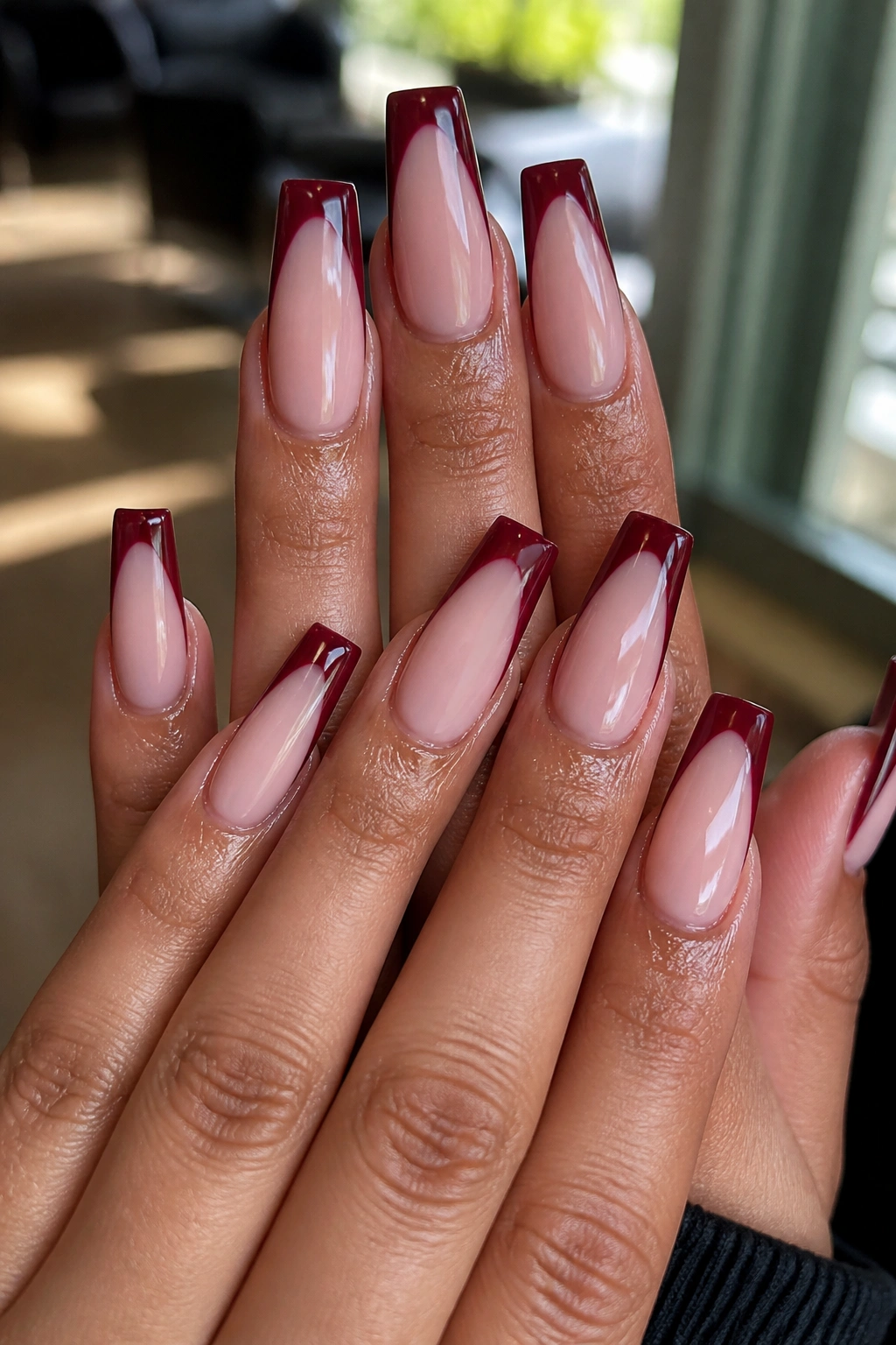 Close-up of hands with dark red French tip coffin nails on milky pink base in a salon
