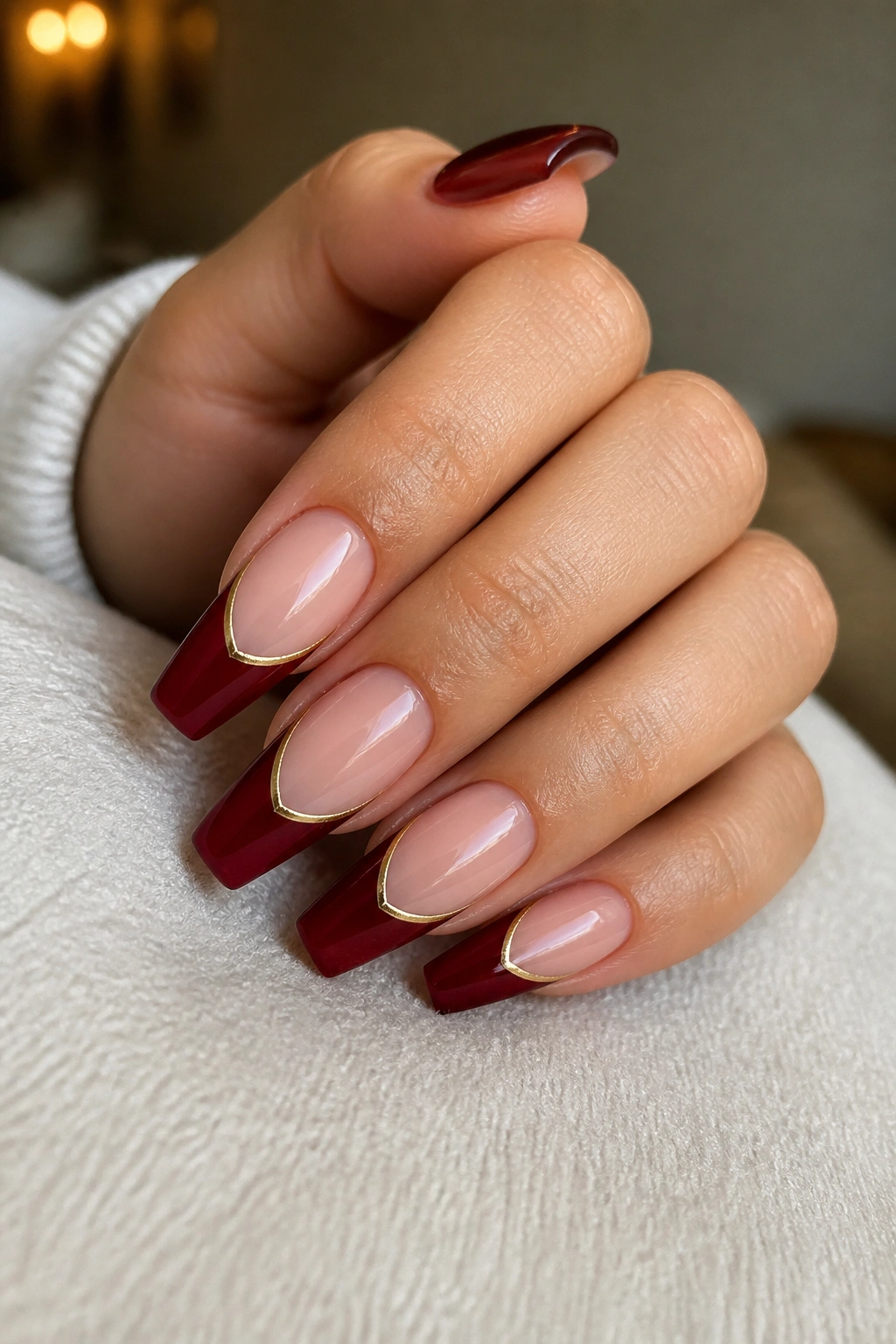 Close-up of a real hand showing dark red coffin nails with a fine gold outline at the tip.