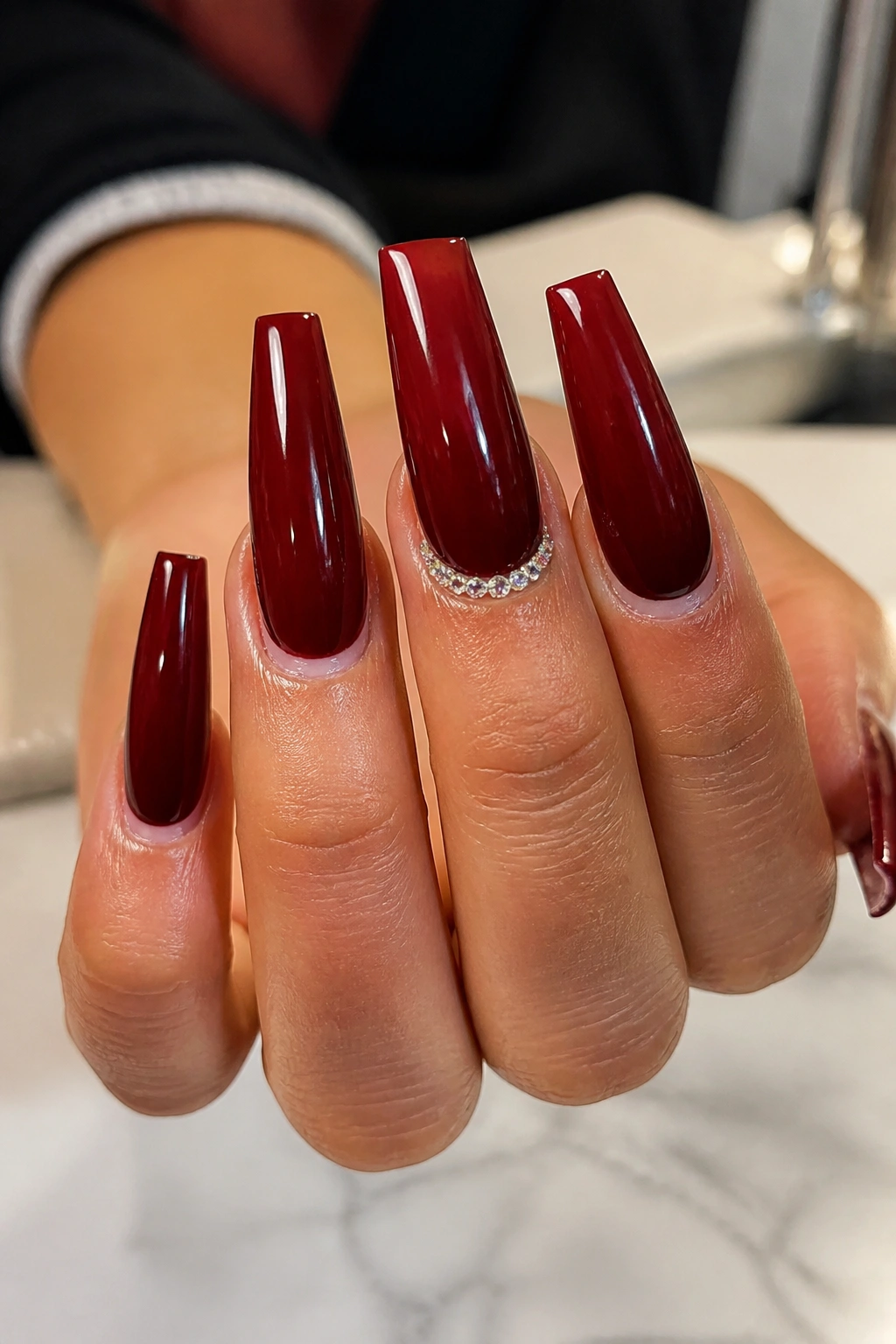 Close-up of nails with a crystal arc on one cuticle nail in a salon setting