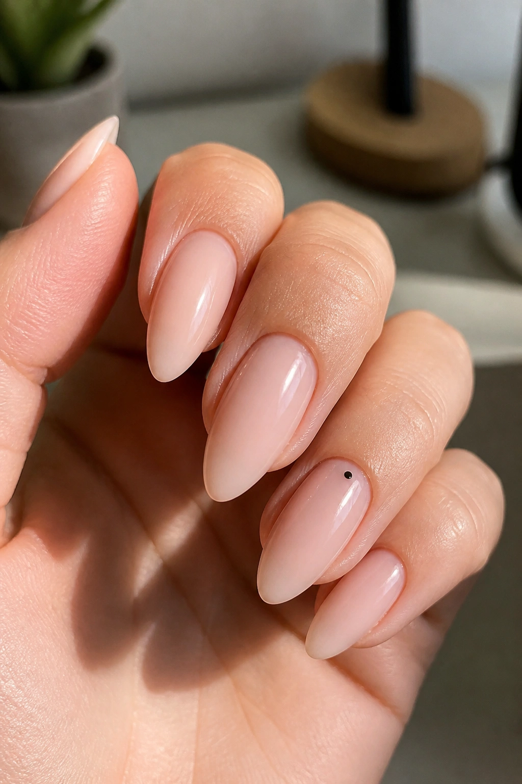 Hand with tiny dot accent on almond nails under soft daylight