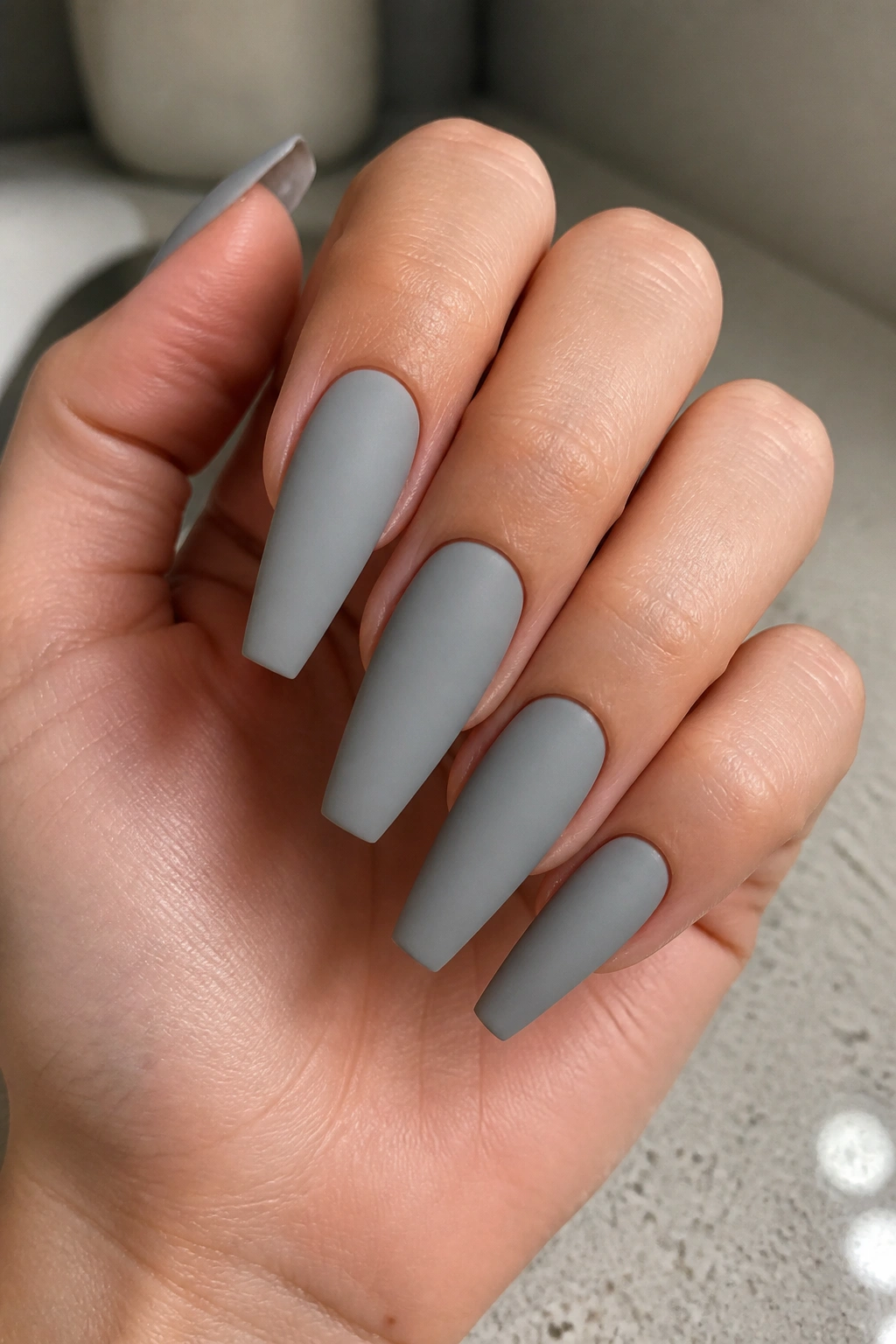 Close-up of a real hand with matte dove grey coffin nails and clean edges