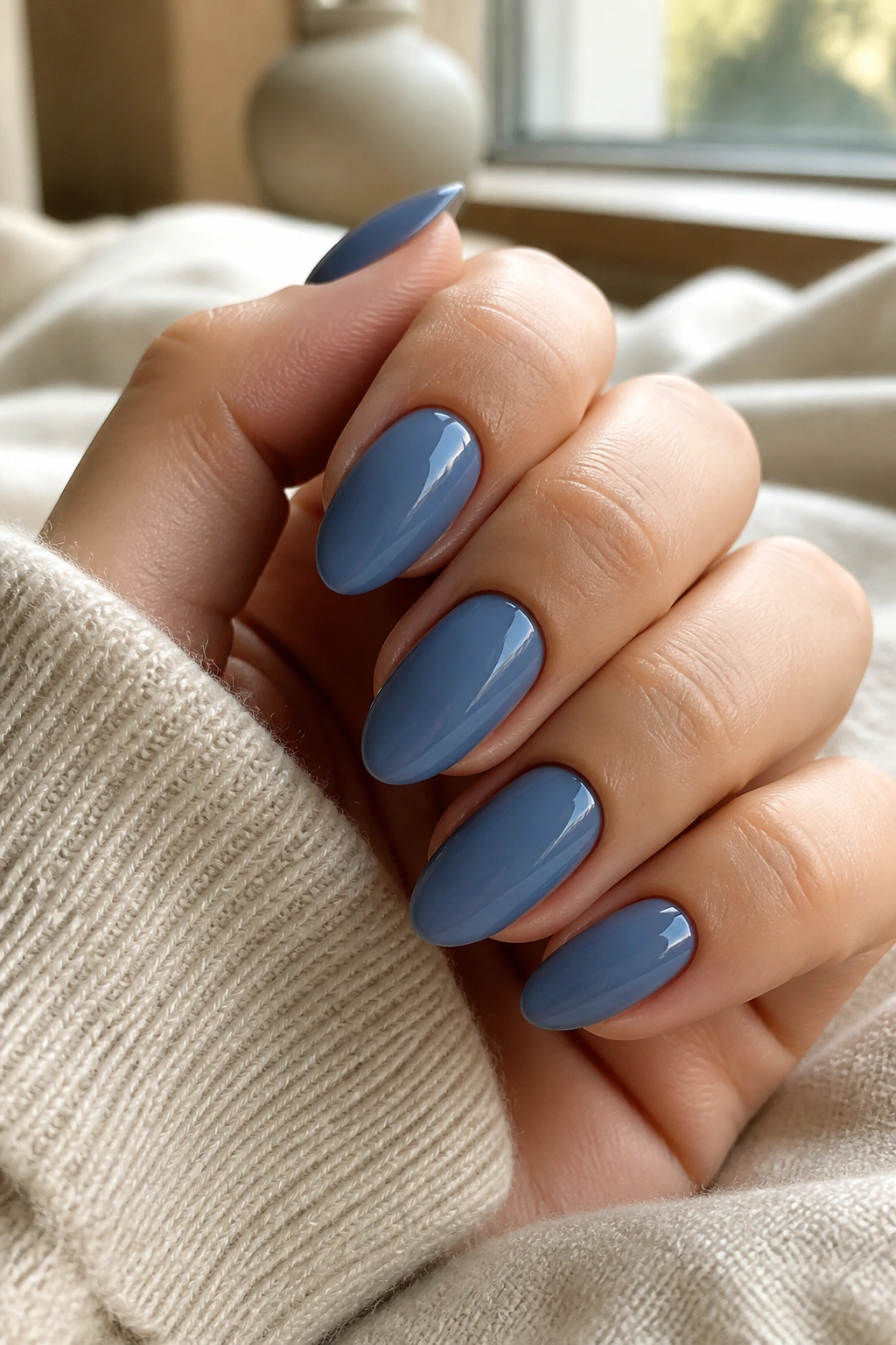 Close-up of almond nails painted dusty slate blue with glossy finish