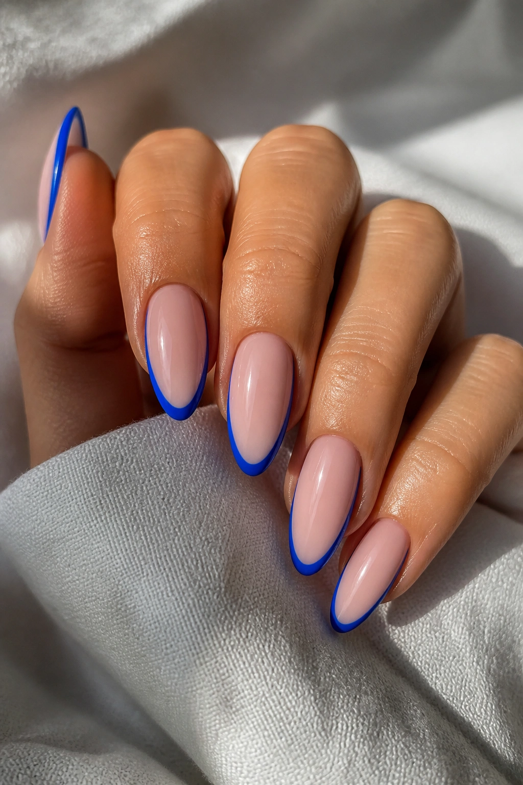 Close-up of almond nails with electric blue outline French on a hand