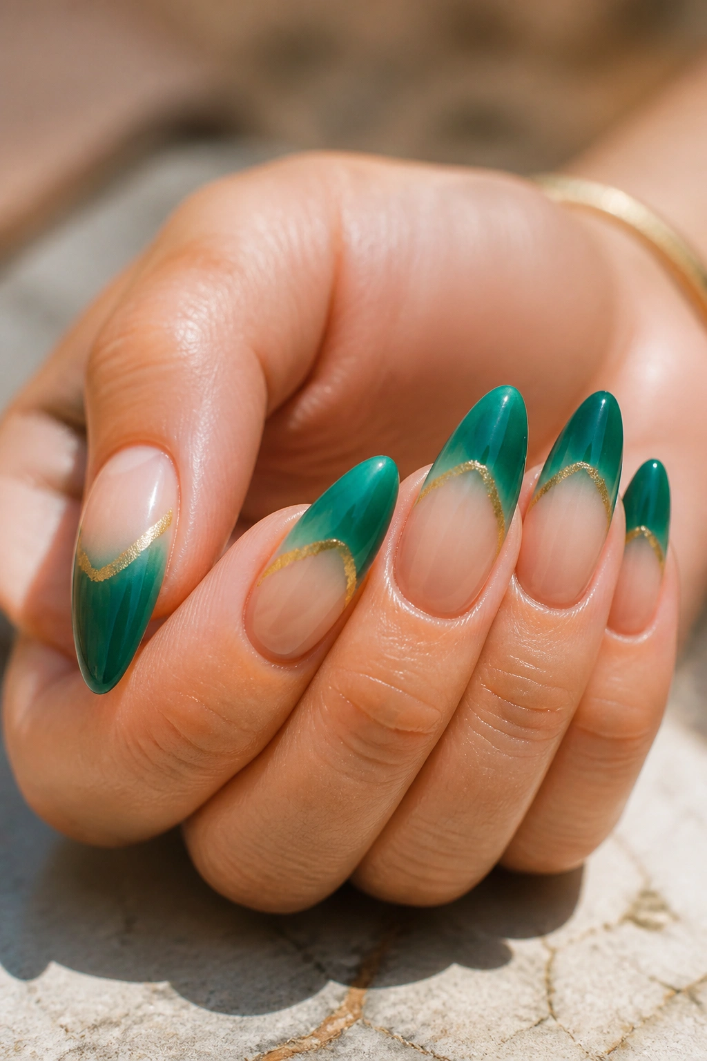 Close-up of emerald and gold ombre almond nails on a real hand