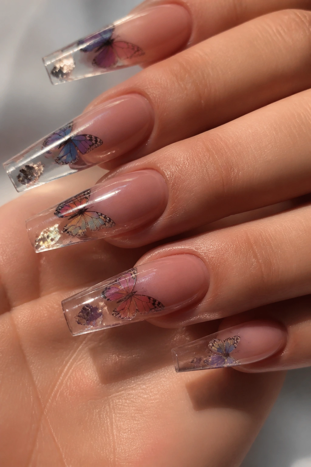 Clear-tip coffin nails with encapsulated butterfly wings on a real hand