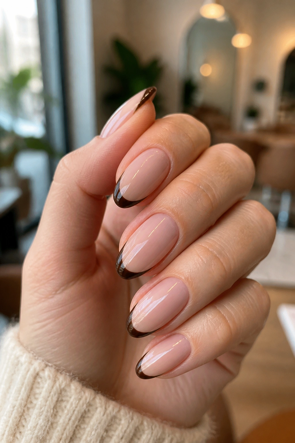 Close-up of almond nails with espresso brown French tips on a sheer pink base