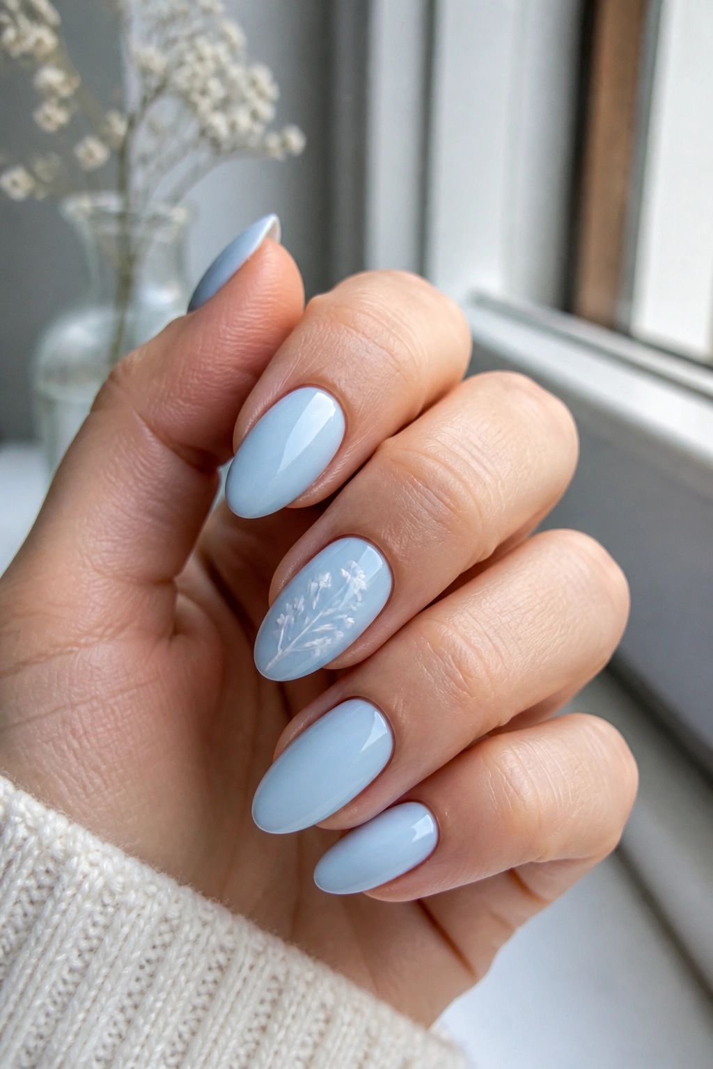 Close-up of almond nails with delicate white floral linework on pastel blue