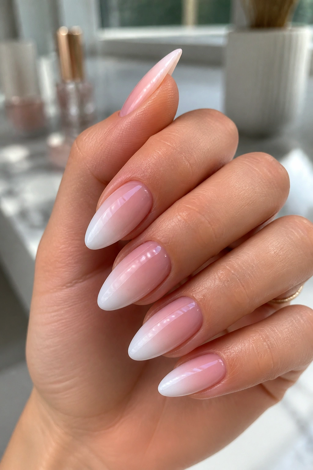 Close-up of long almond nails with a soft pink-to-white French fade on a real hand.