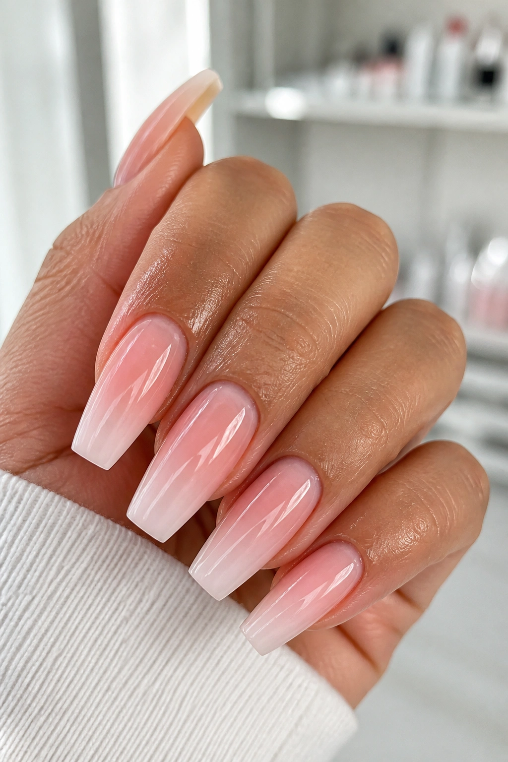 Close-up of French fade pink ombre coffin nails with glossy nude base on a real hand