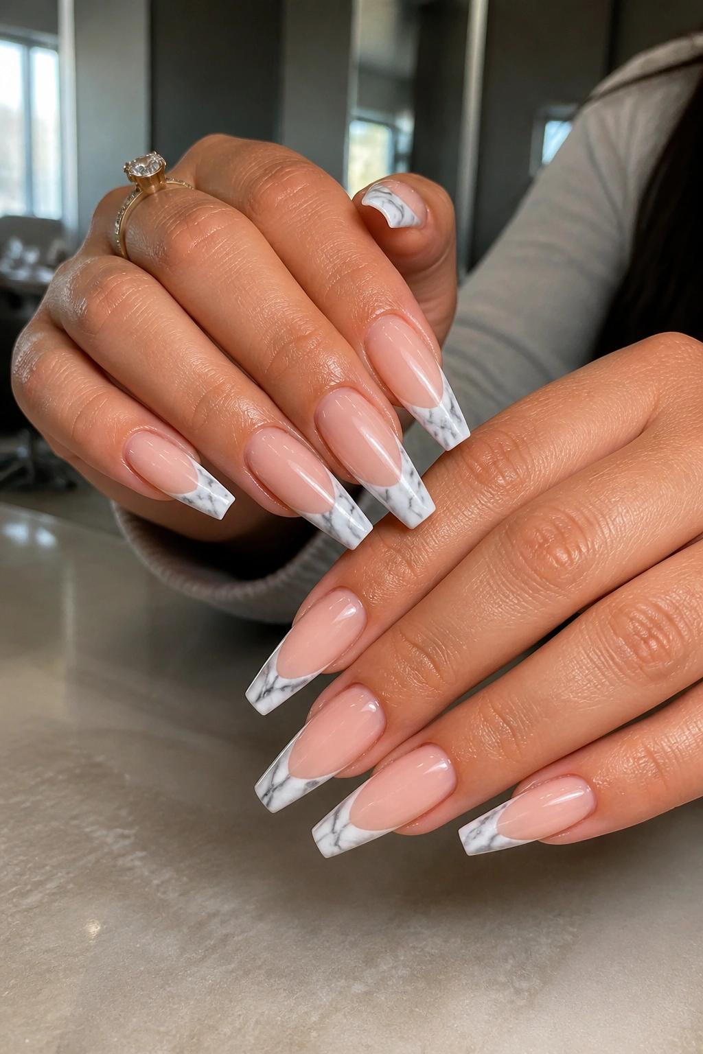 Close-up of nude-based coffin nails with white-gray marble French tips on a real person's hands in a salon setting