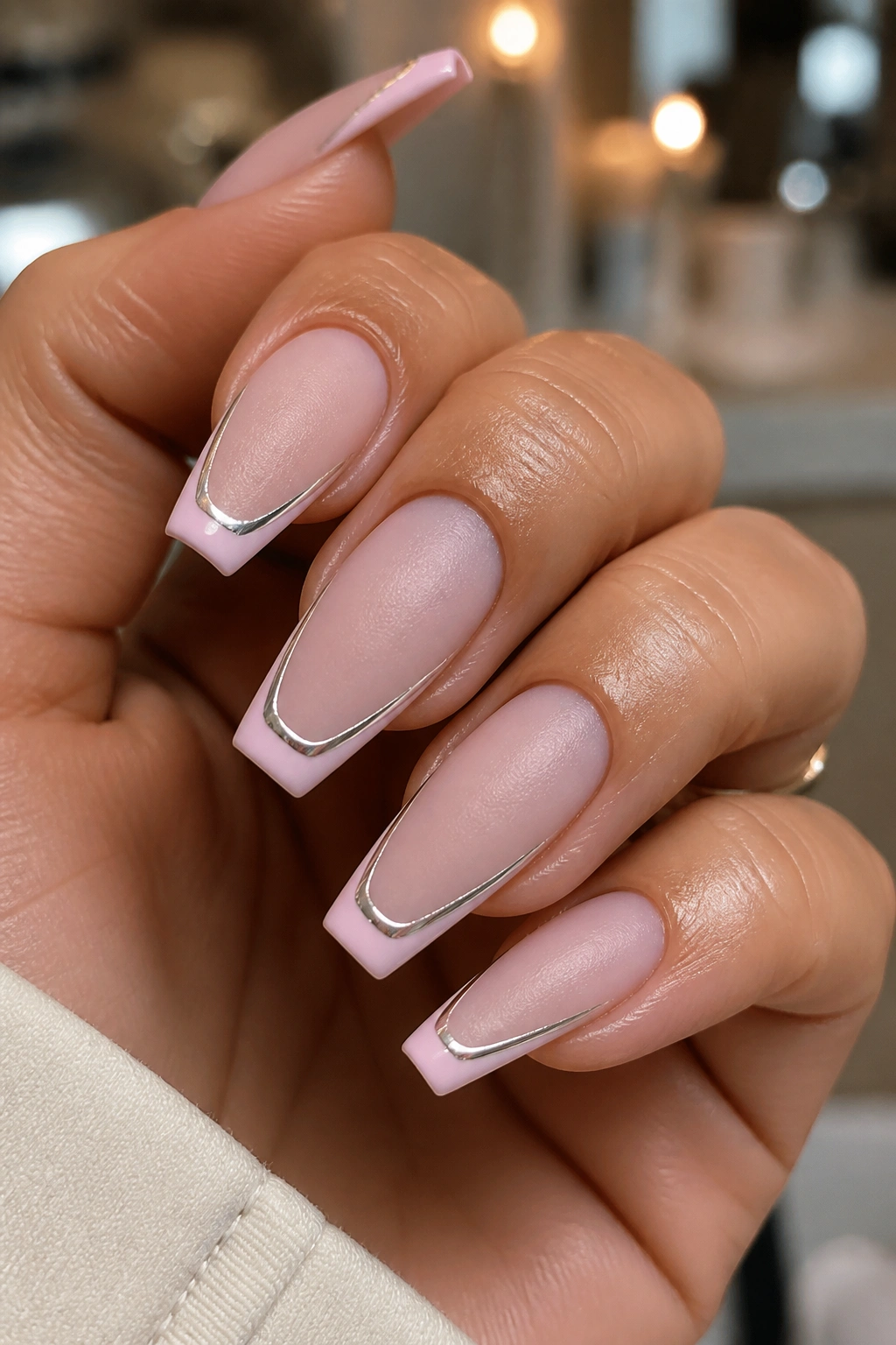 Close-up of coffin nails with frosted pink French tips and chrome edges on a real hand