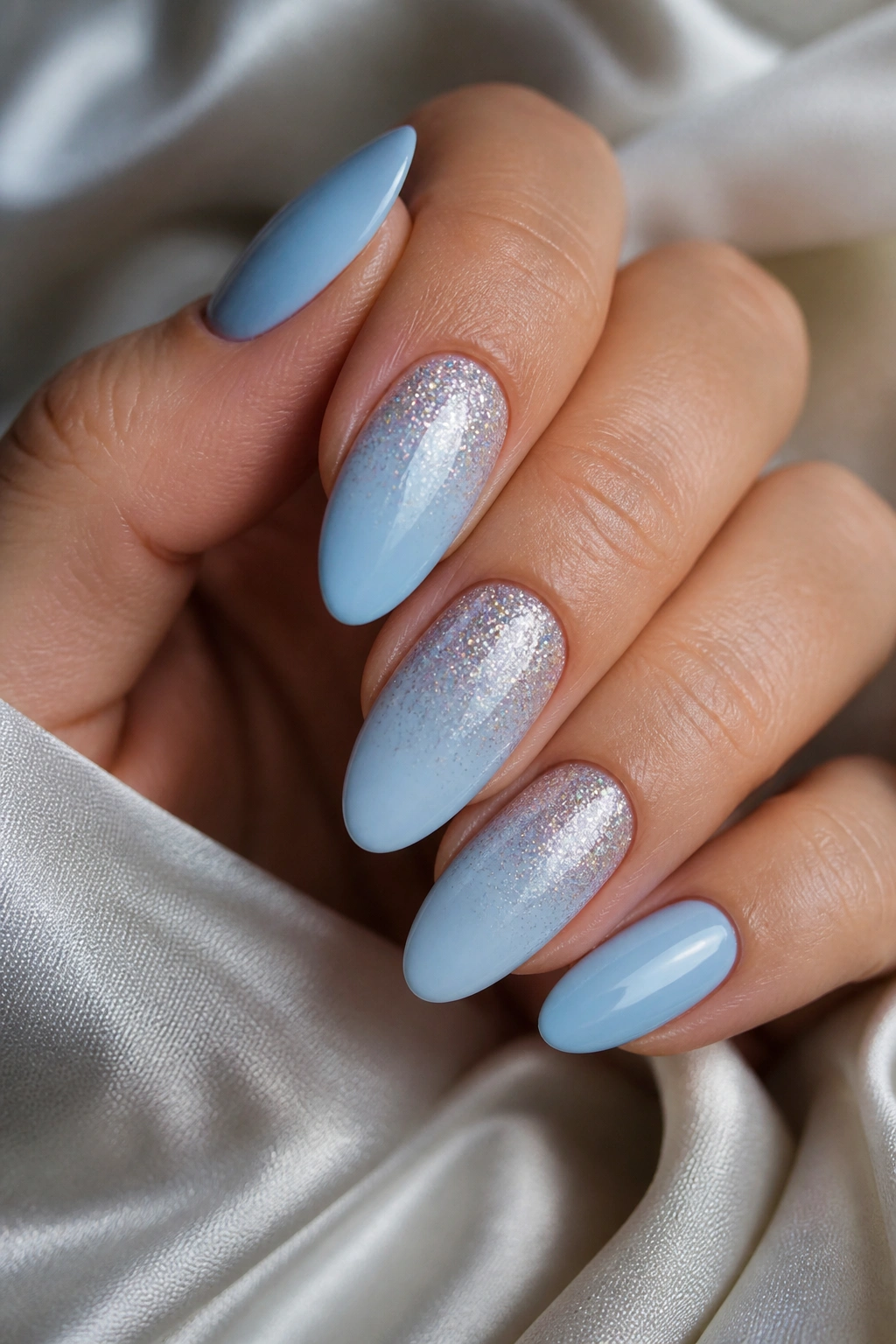 Close-up of almond nails with glitter fade on light blue polish