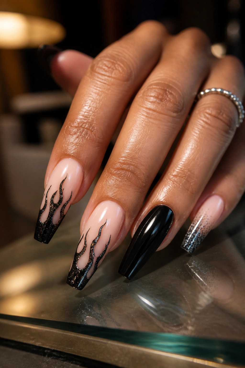 Nails with black glitter flame design on a nude base close-up