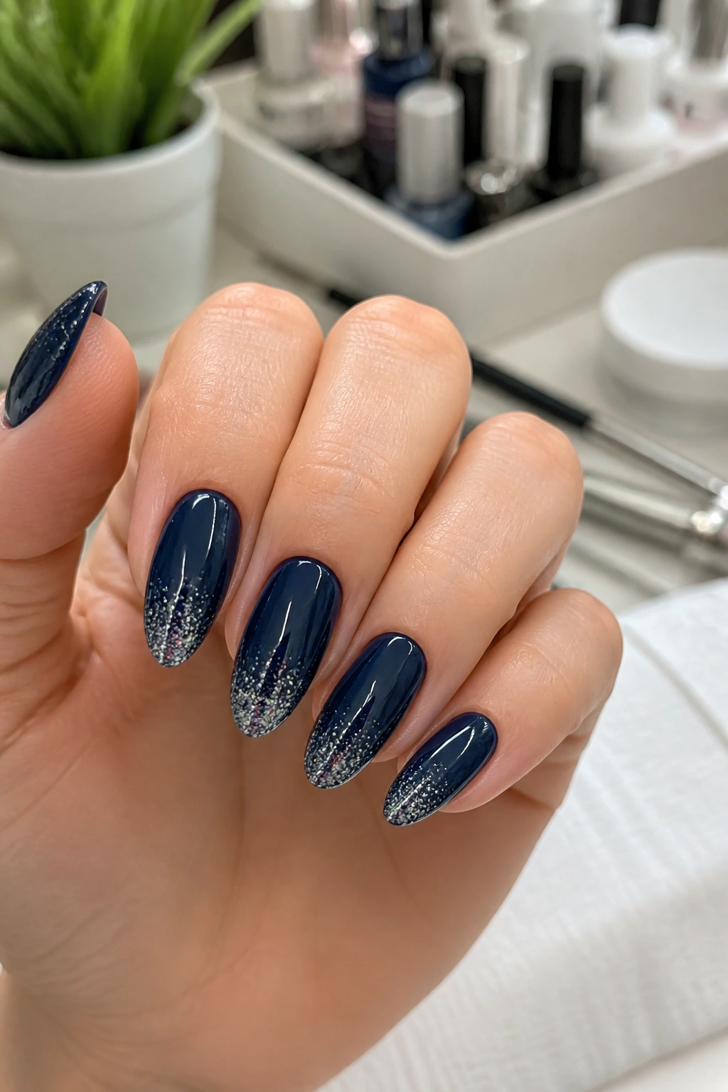 Almond nails with glitter gradient navy tips in a salon setting