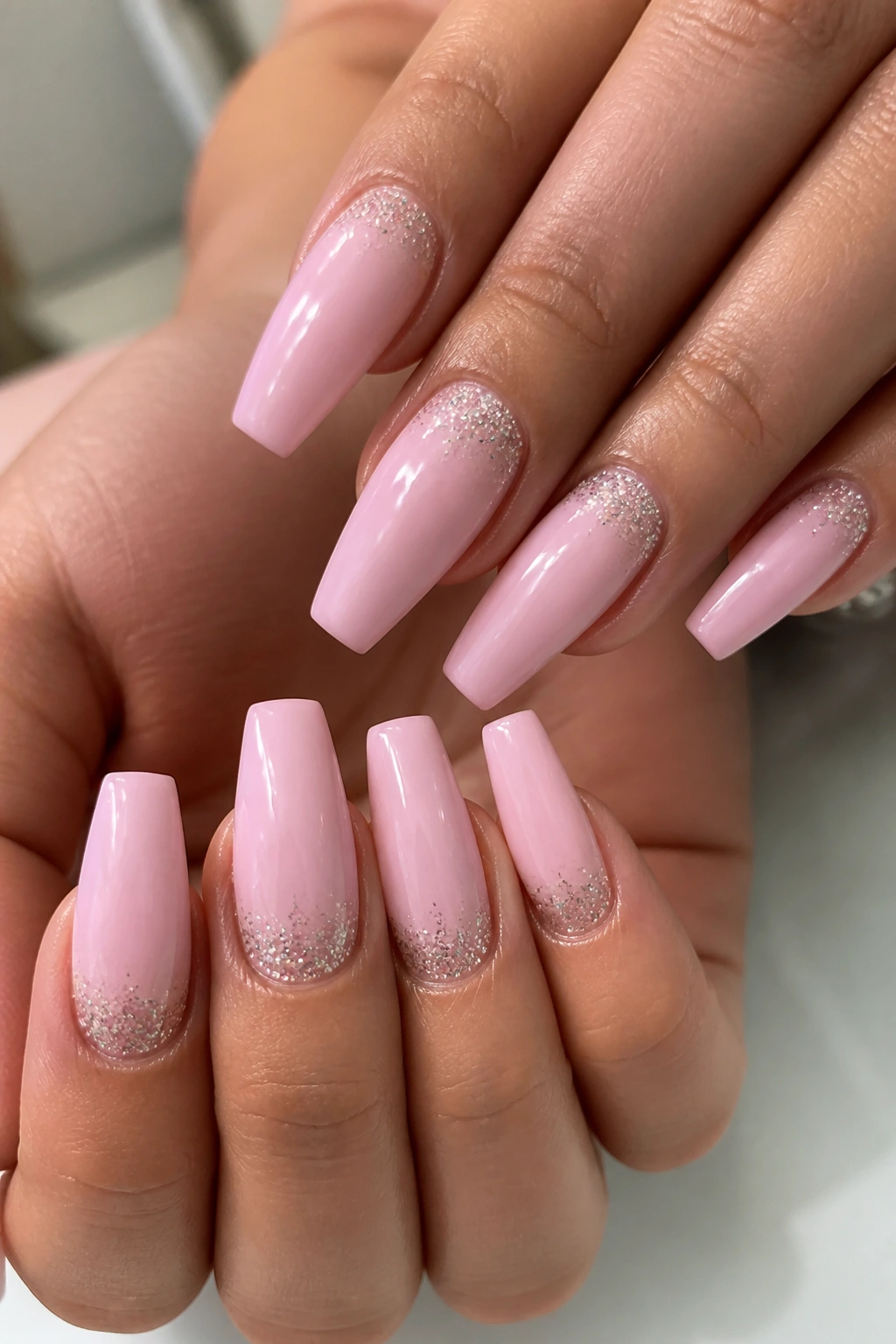 Close-up of light pink coffin nails with cuticle glitter dust on real hands