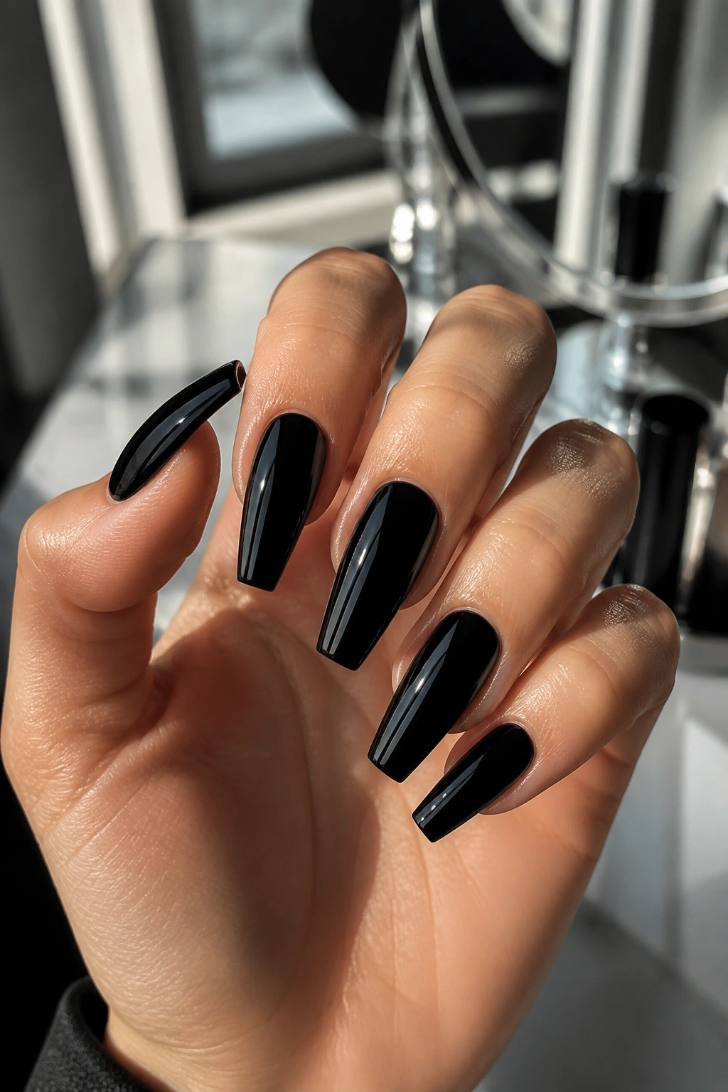 Close-up of glossy black coffin nails with a patent finish on a hand.