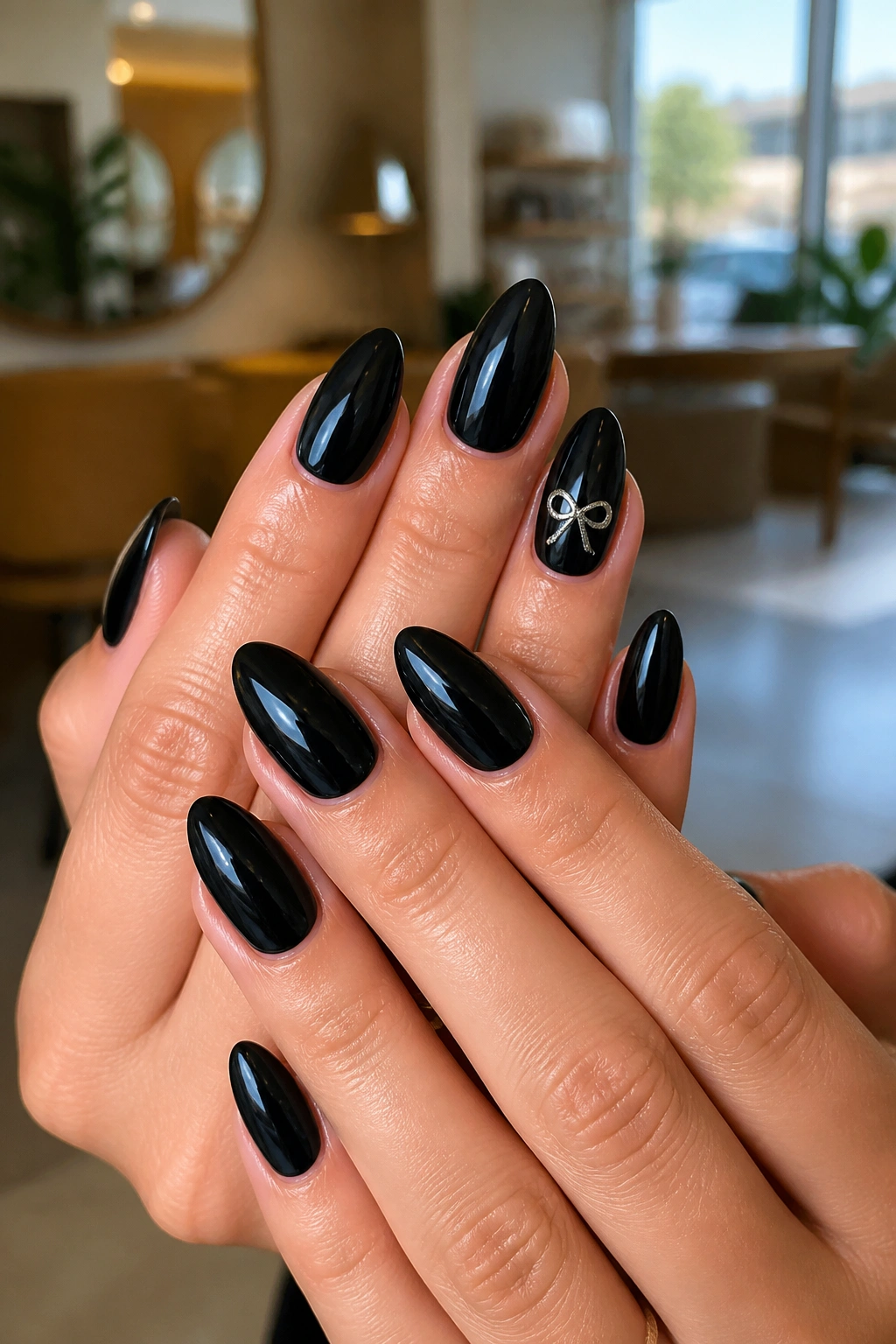 Close-up of glossy black almond nails with a slim silver bow on the ring finger