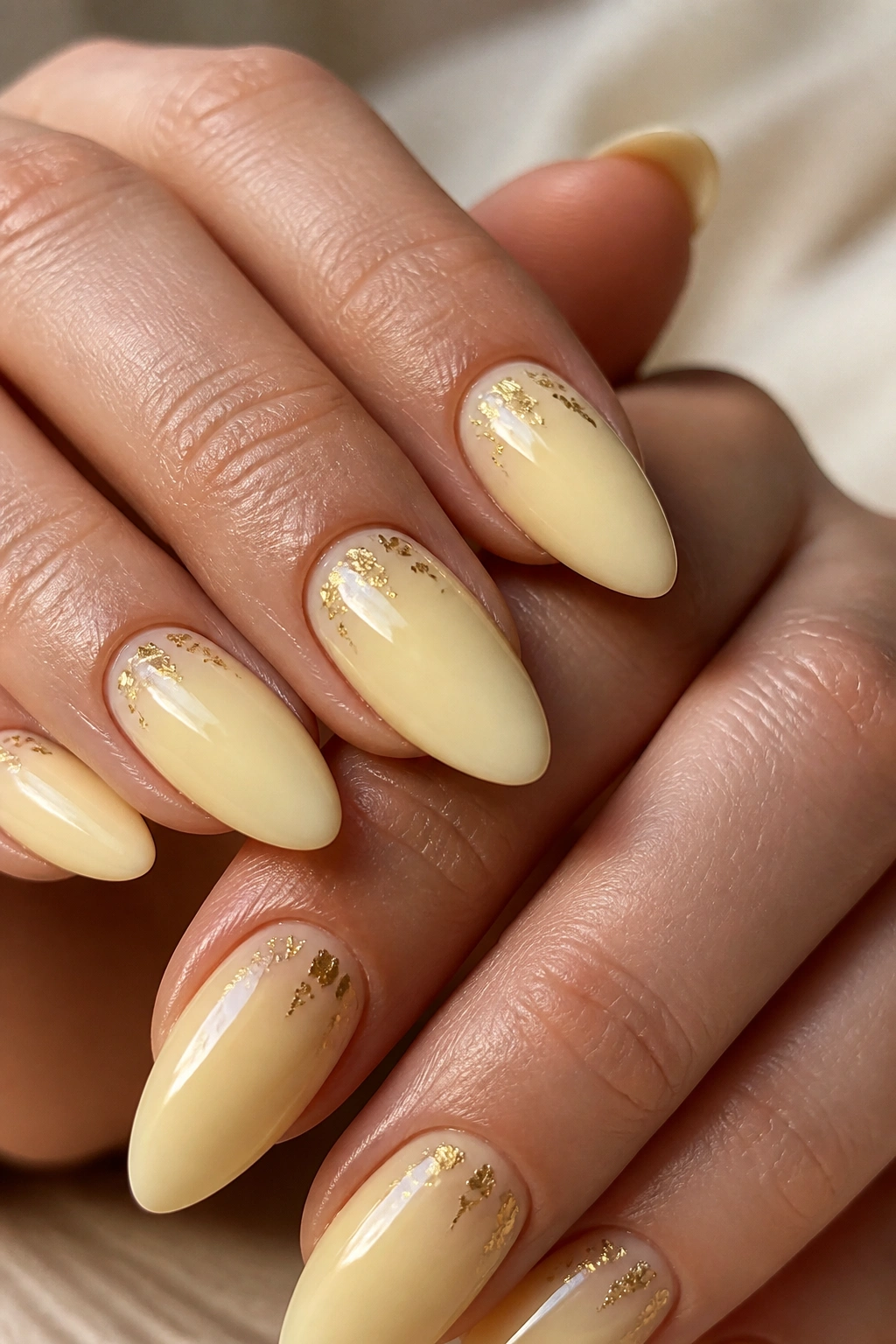 Almond nails with gold foil flecks on a butter-yellow base