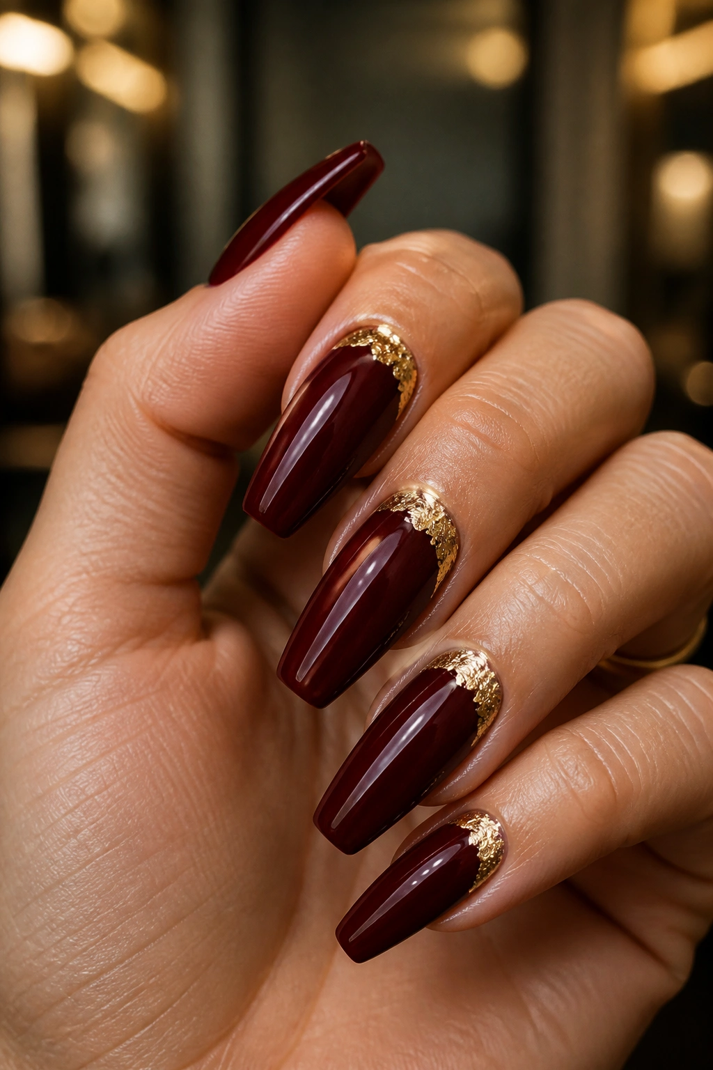 Close-up of deep maroon coffin nails with gold foil near the cuticle