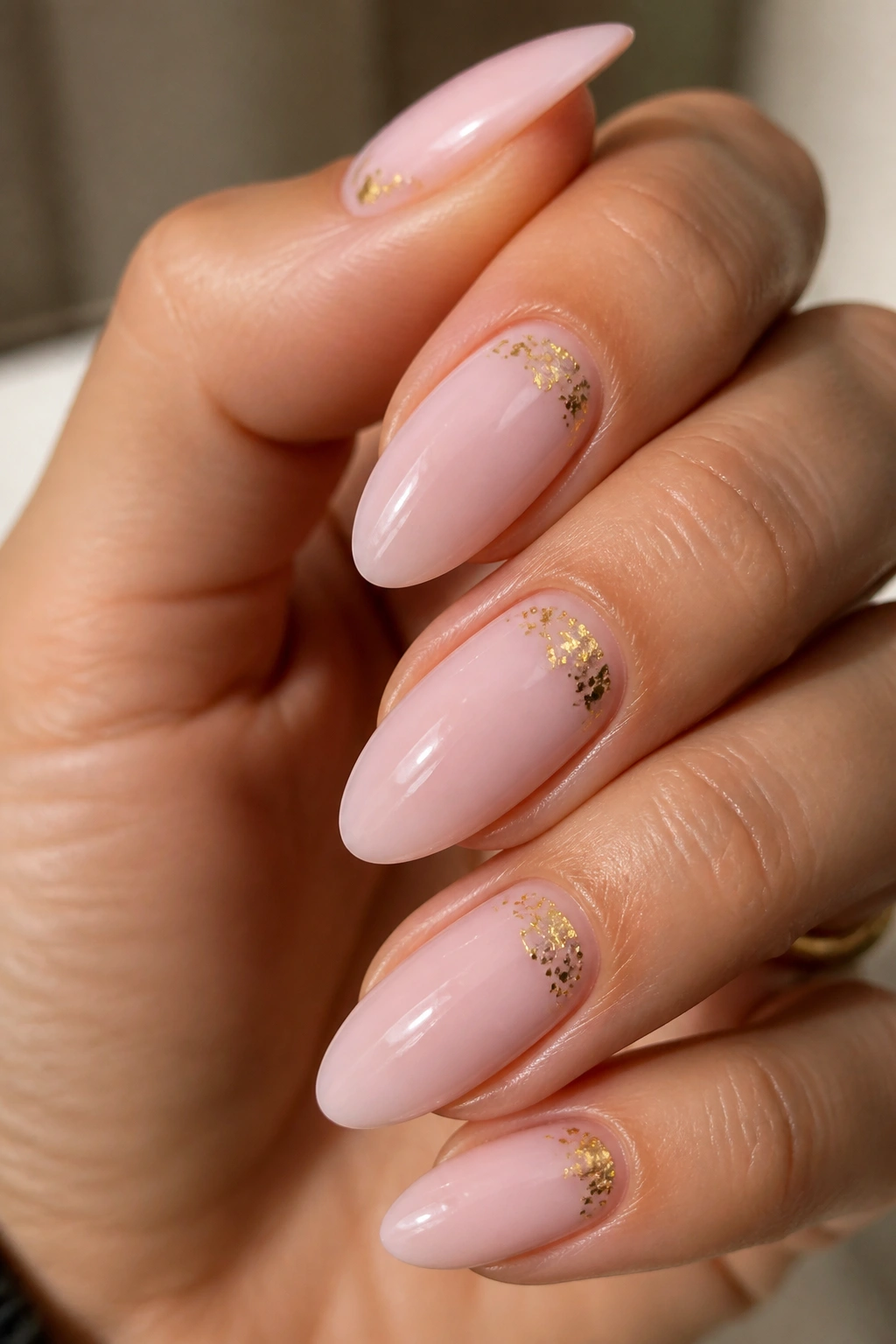 Close-up light pink almond nails with tiny gold foil specks