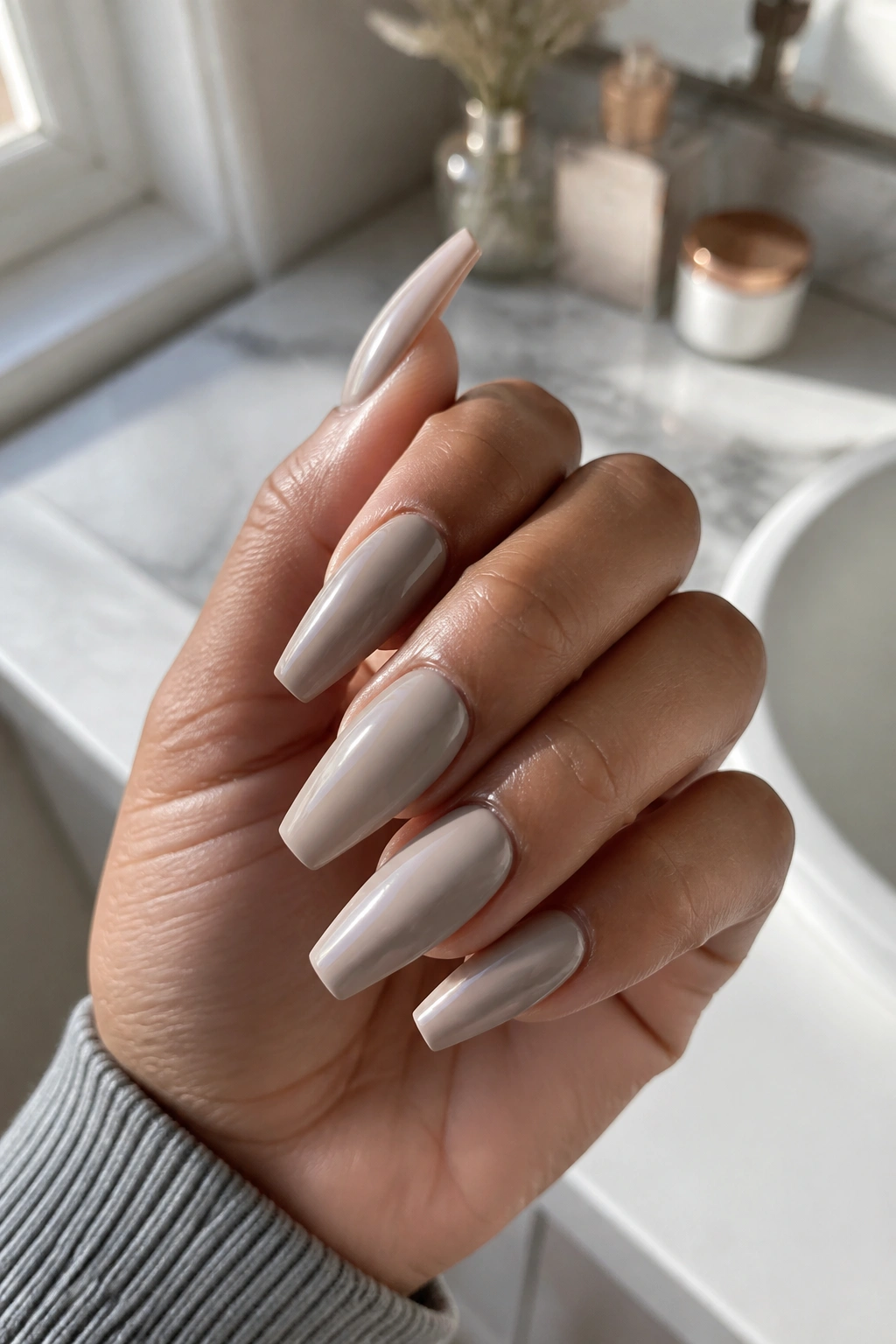 Close-up of a real hand with greige coffin nails at medium length in daylight